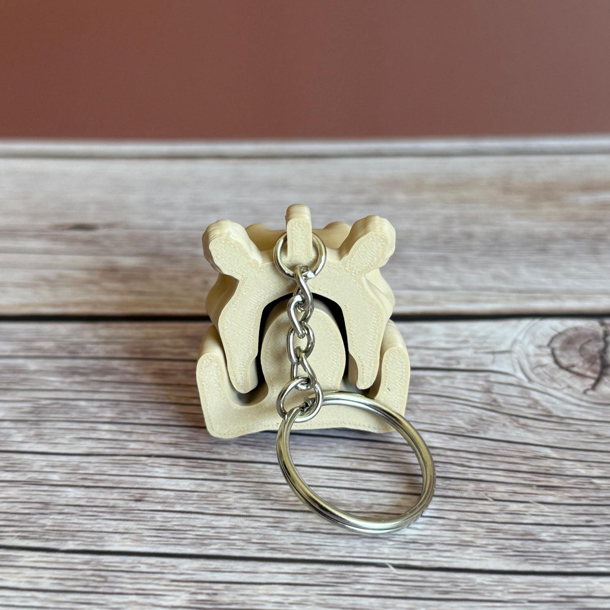 Back of 3D printed beige hippo skull keychain, placed on a wooden surface with a brown background