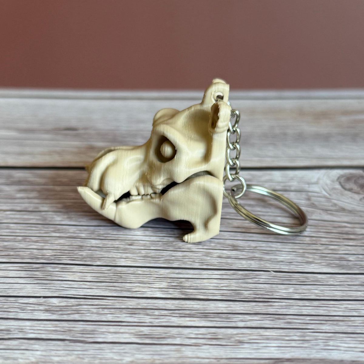 Side of 3D printed beige hippo skull keychain, placed on a wooden surface with a brown background