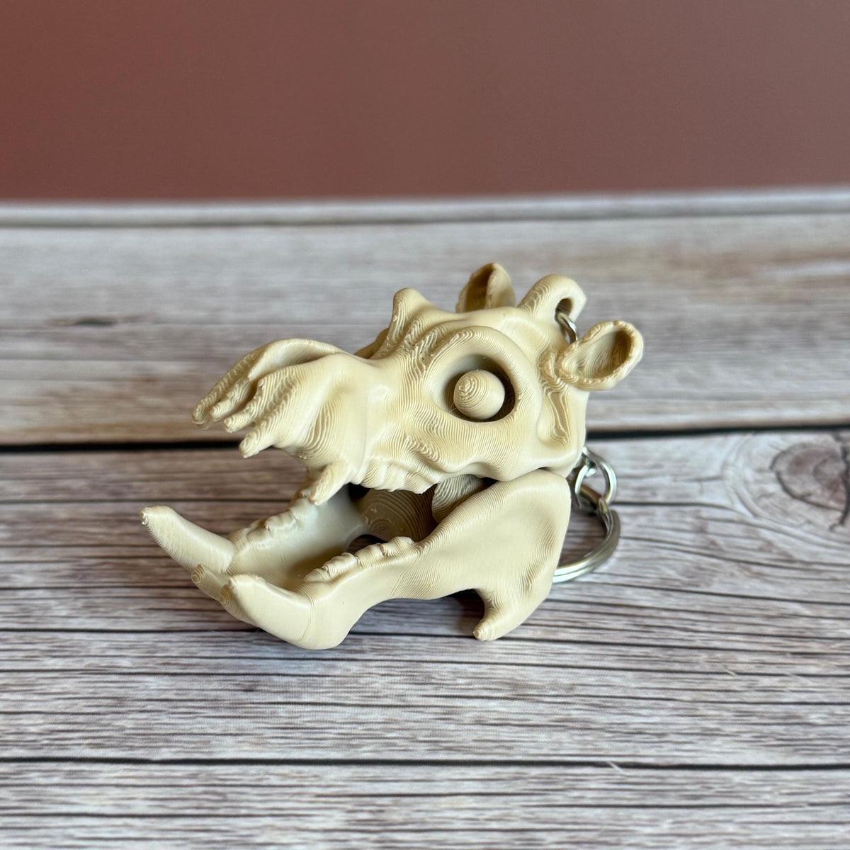 Side of 3D printed beige hippo skull keychain with mouth open, placed on a wooden surface with a brown background