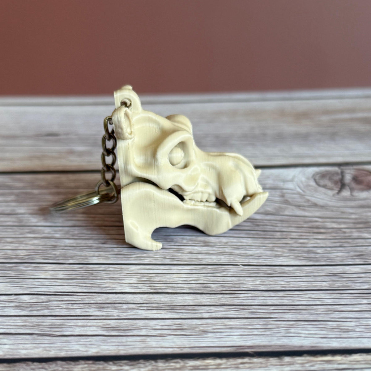 Side of 3D printed beige hippo skull keychain, placed on a wooden surface with a brown background