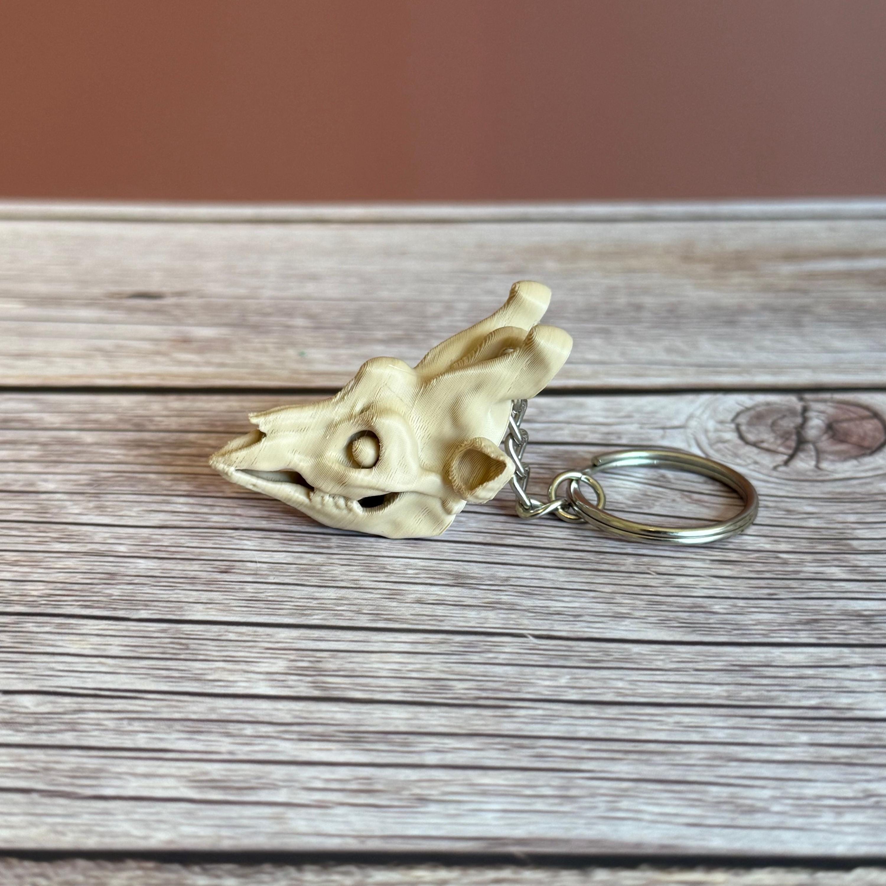 side of 3D printed beige giraffe skull keychain, placed on a wooden surface and brown background
