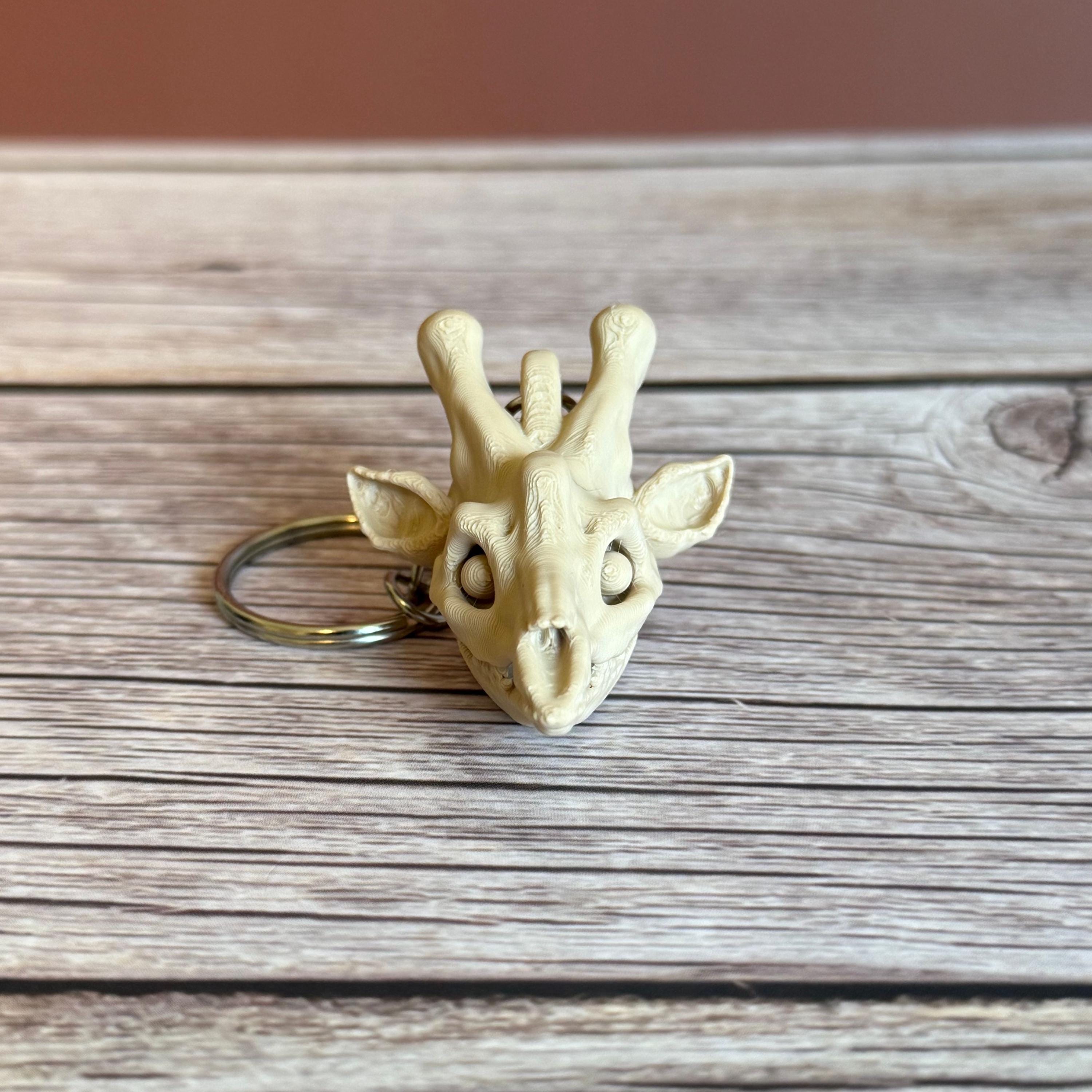 front of 3D printed beige giraffe skull keychain, placed on a wooden surface and brown background