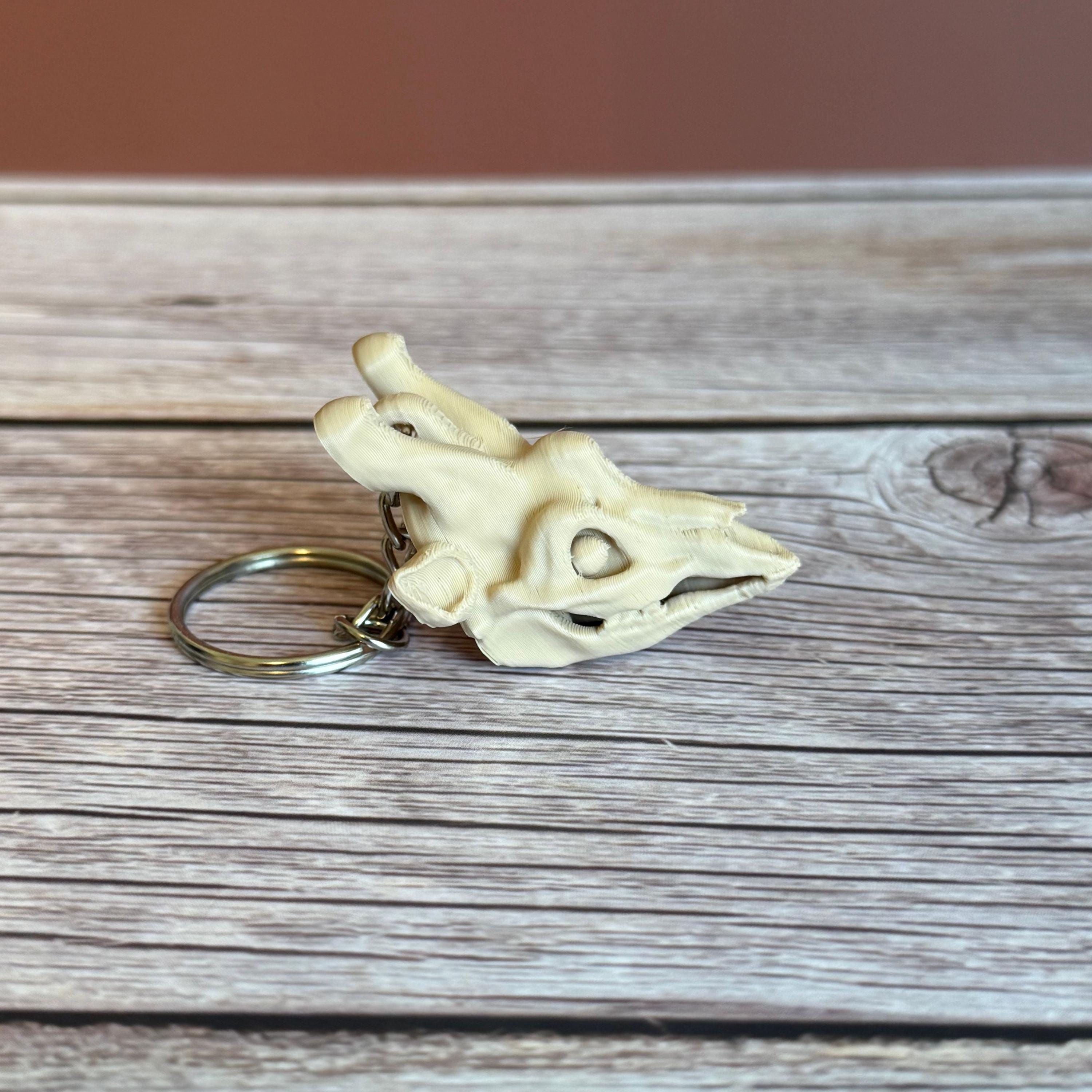 side of 3D printed beige giraffe skull keychain, placed on a wooden surface and brown background