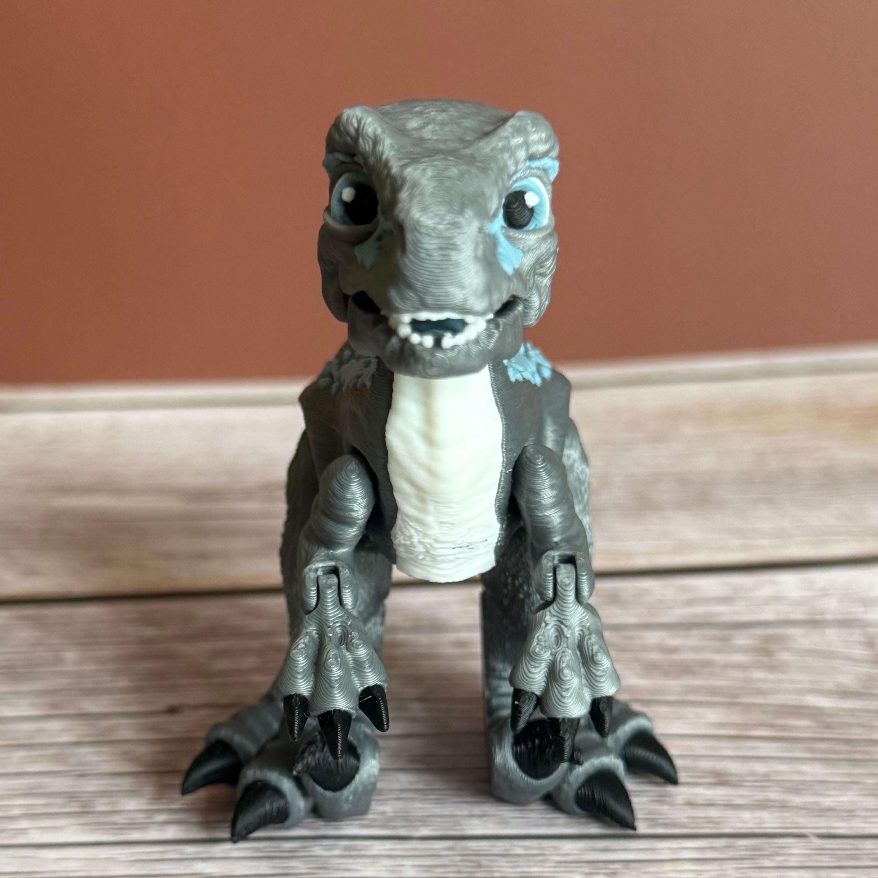 Front of a 3D printed blue, gray, and white colored raptor dinosaur figure, placed on a wooden surface against a brown background
