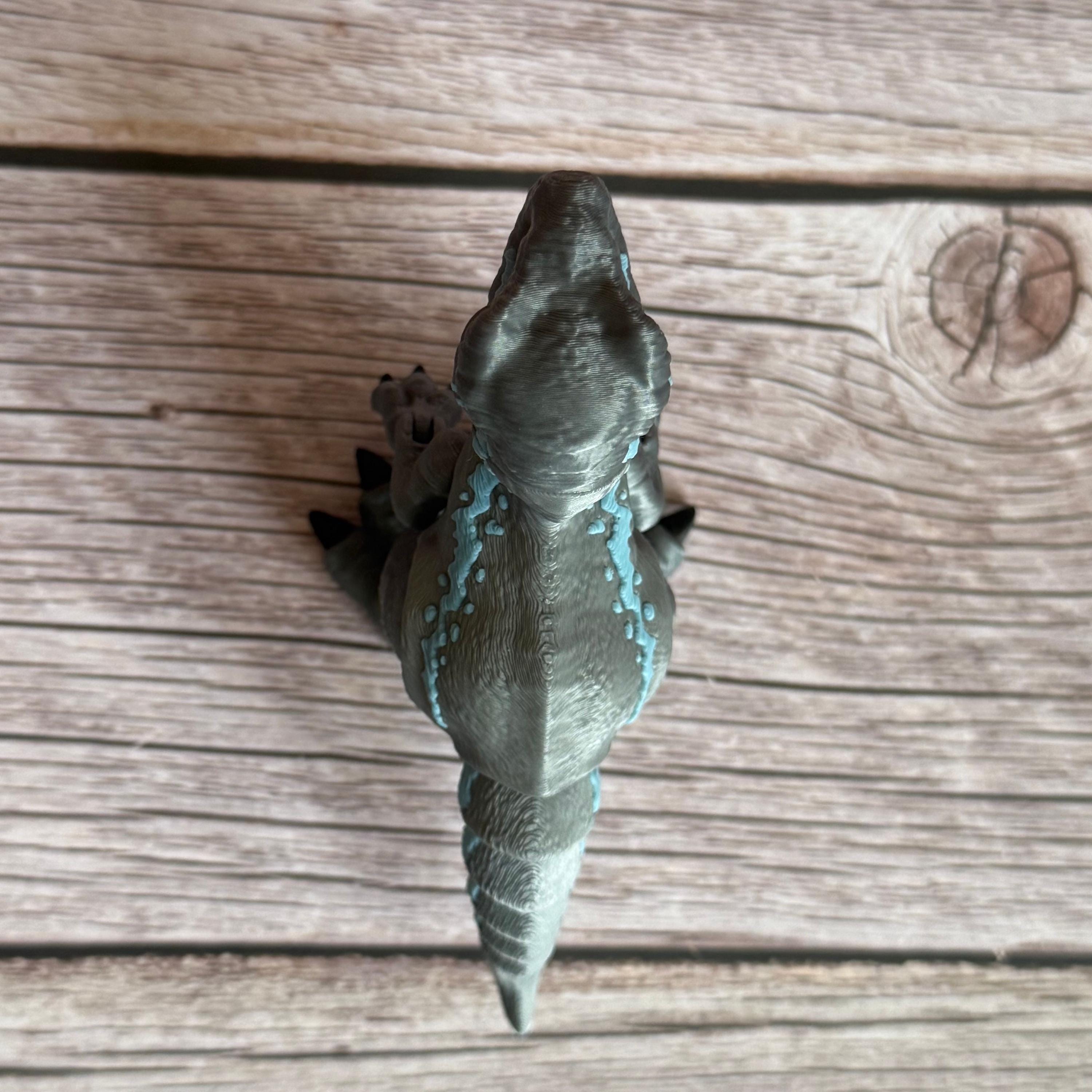 Top of a 3D printed blue, gray, and white colored raptor dinosaur figure, placed on a wooden surface