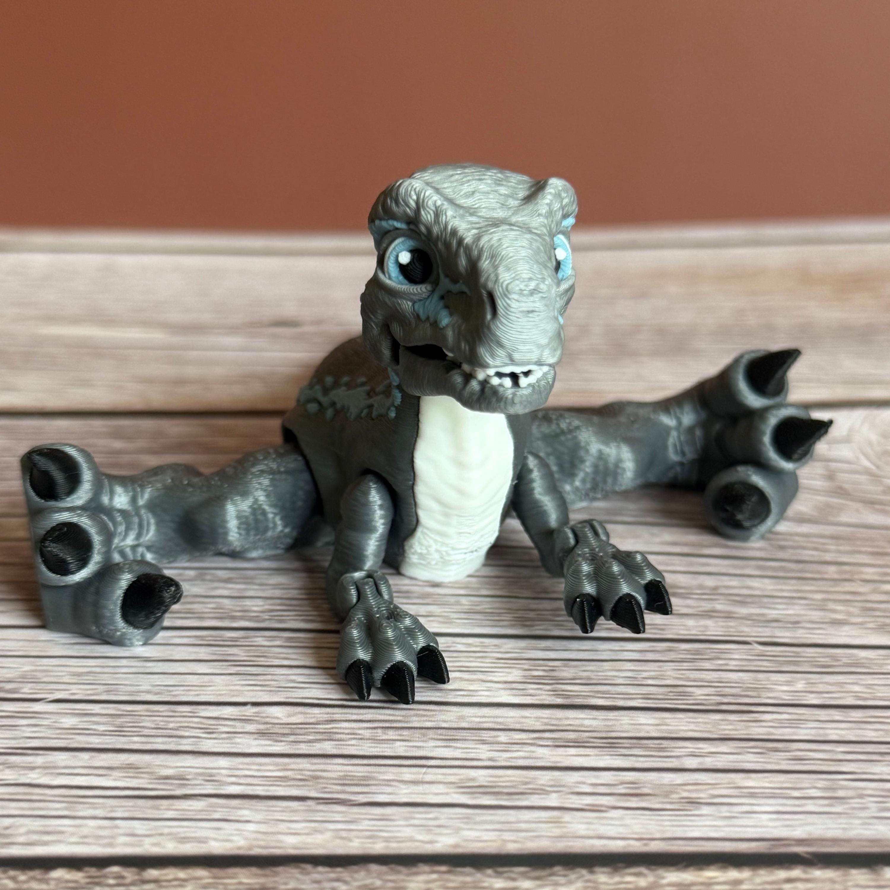 Front of a 3D printed blue, gray, and white colored raptor dinosaur figure with legs spread wide, placed on a wooden surface against a brown background