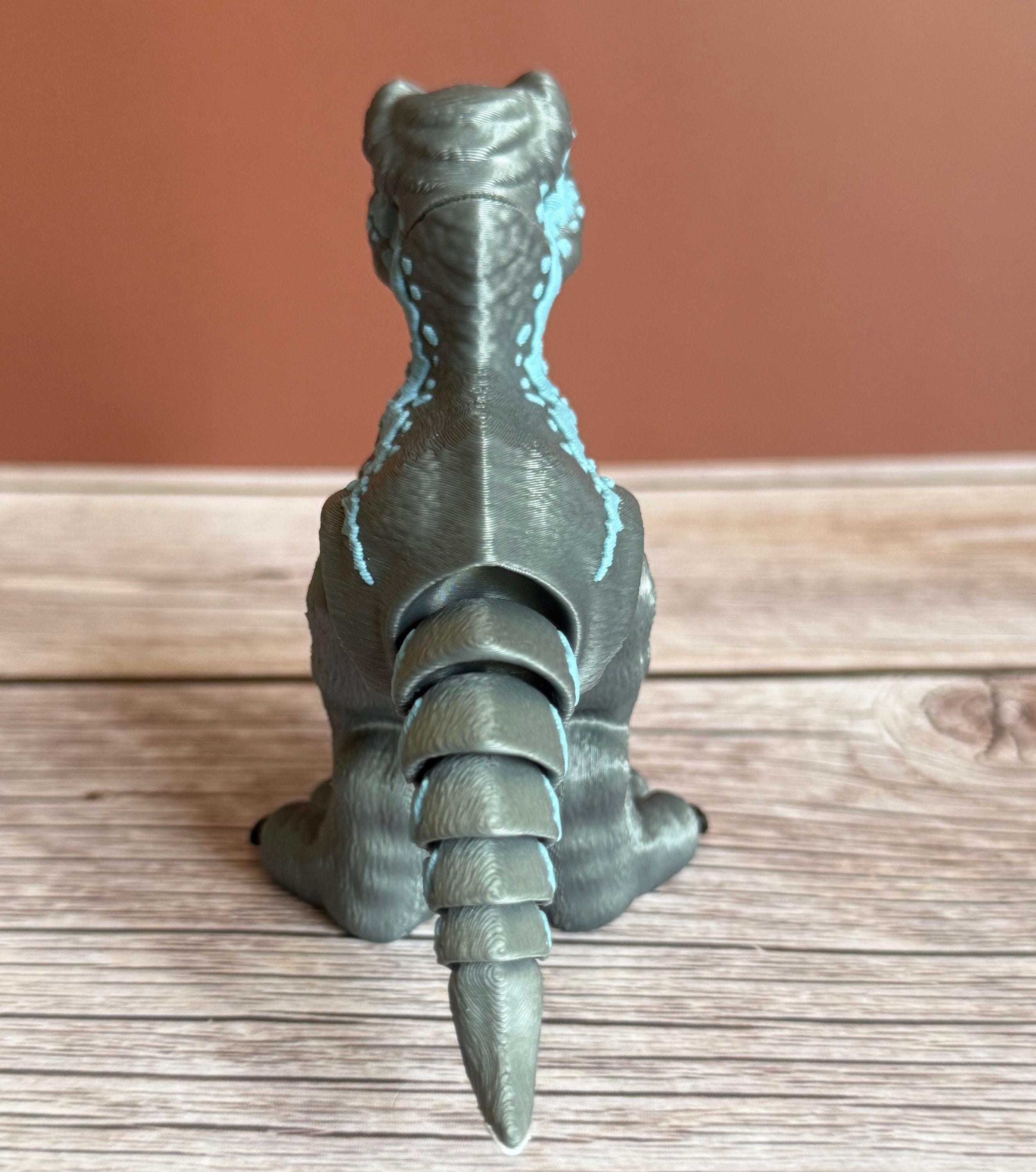 Back of a 3D printed blue, gray, and white colored raptor dinosaur figure, placed on a wooden surface against a brown background