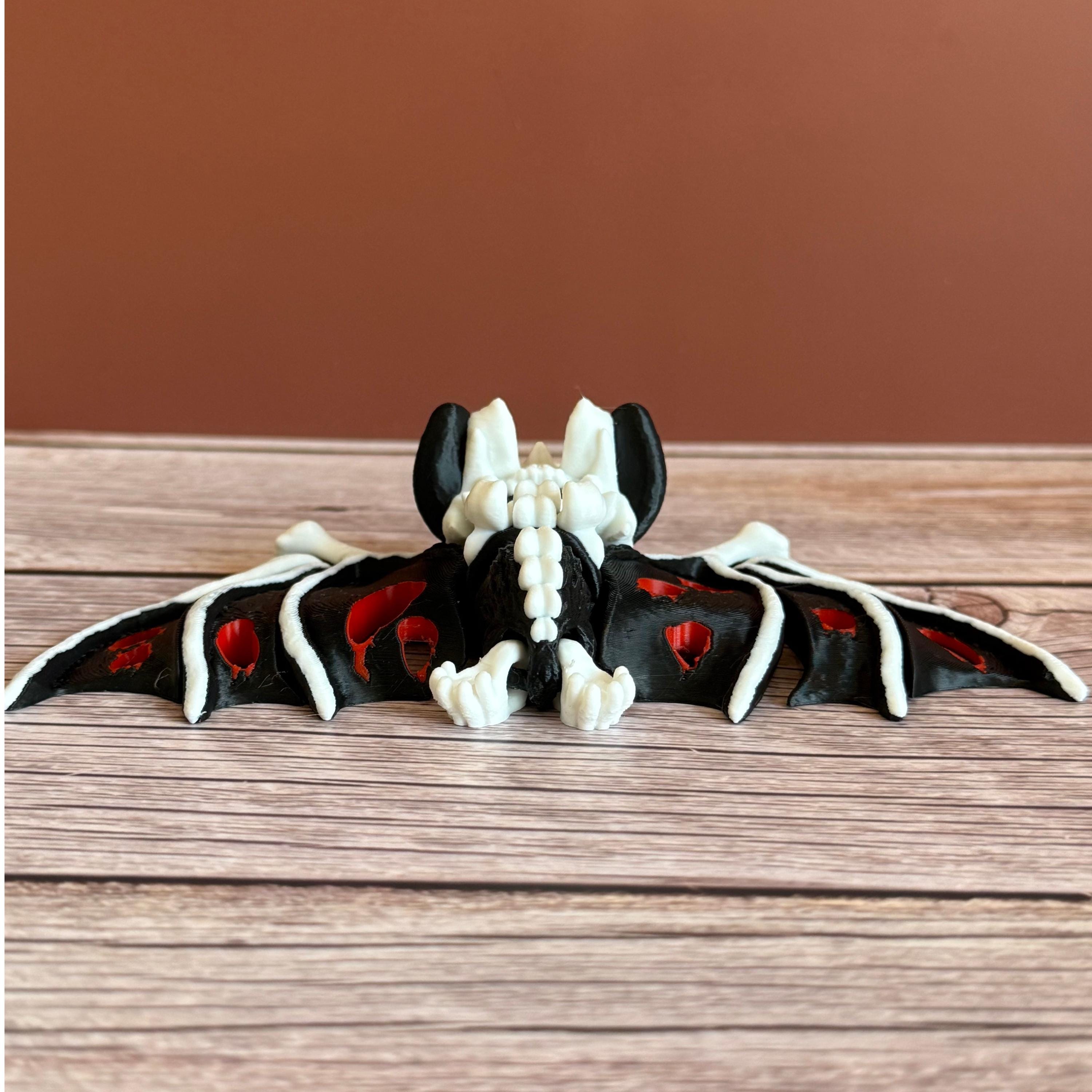 Back of a 3D printed skeleton-like bat with bloody appearing wings and red eyes, placed on a wooden surface and brown background