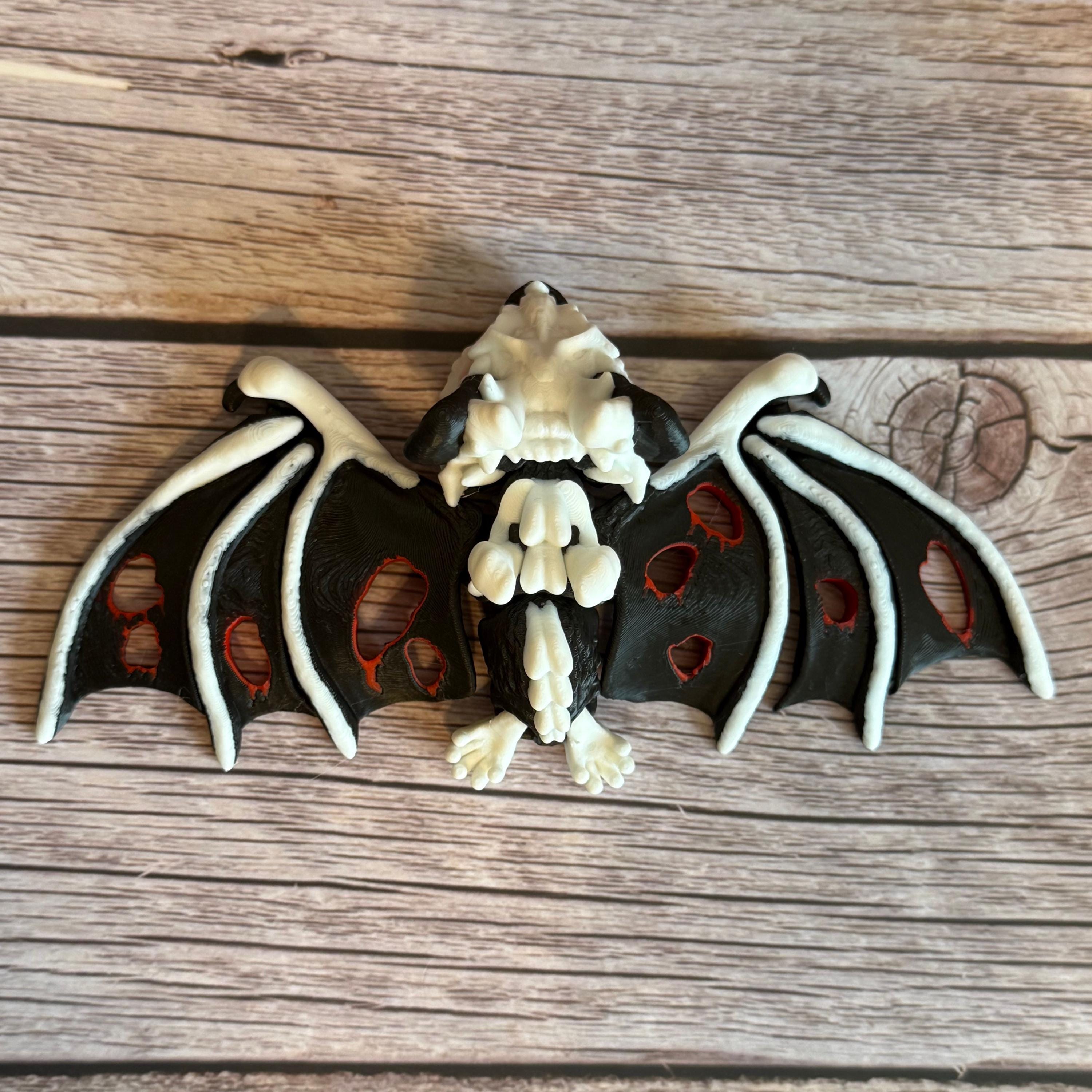 Top of a 3D printed skeleton-like bat with bloody appearing wings, placed on a wooden surface 