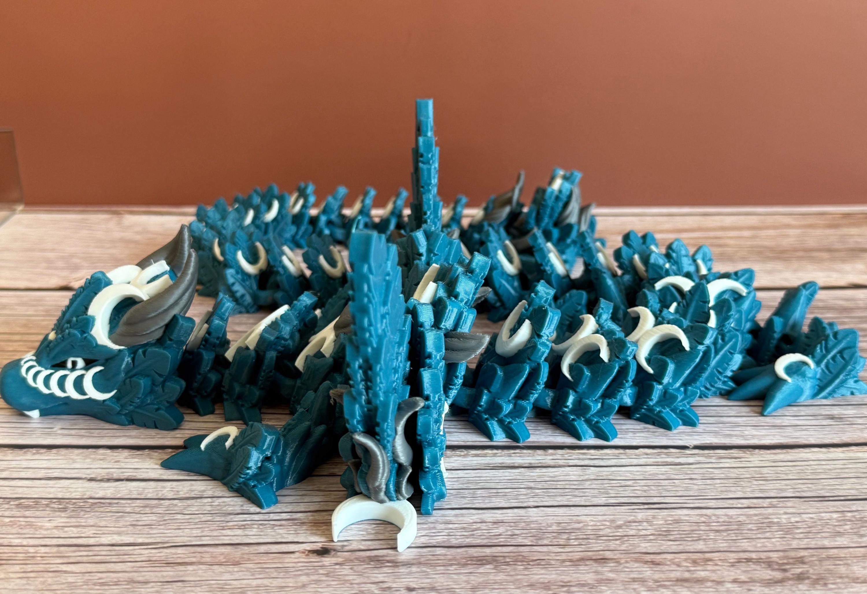 Side of a 3D printed, blue articulated dragon toy with white celestial-inspired patterns, placed on a wooden surface