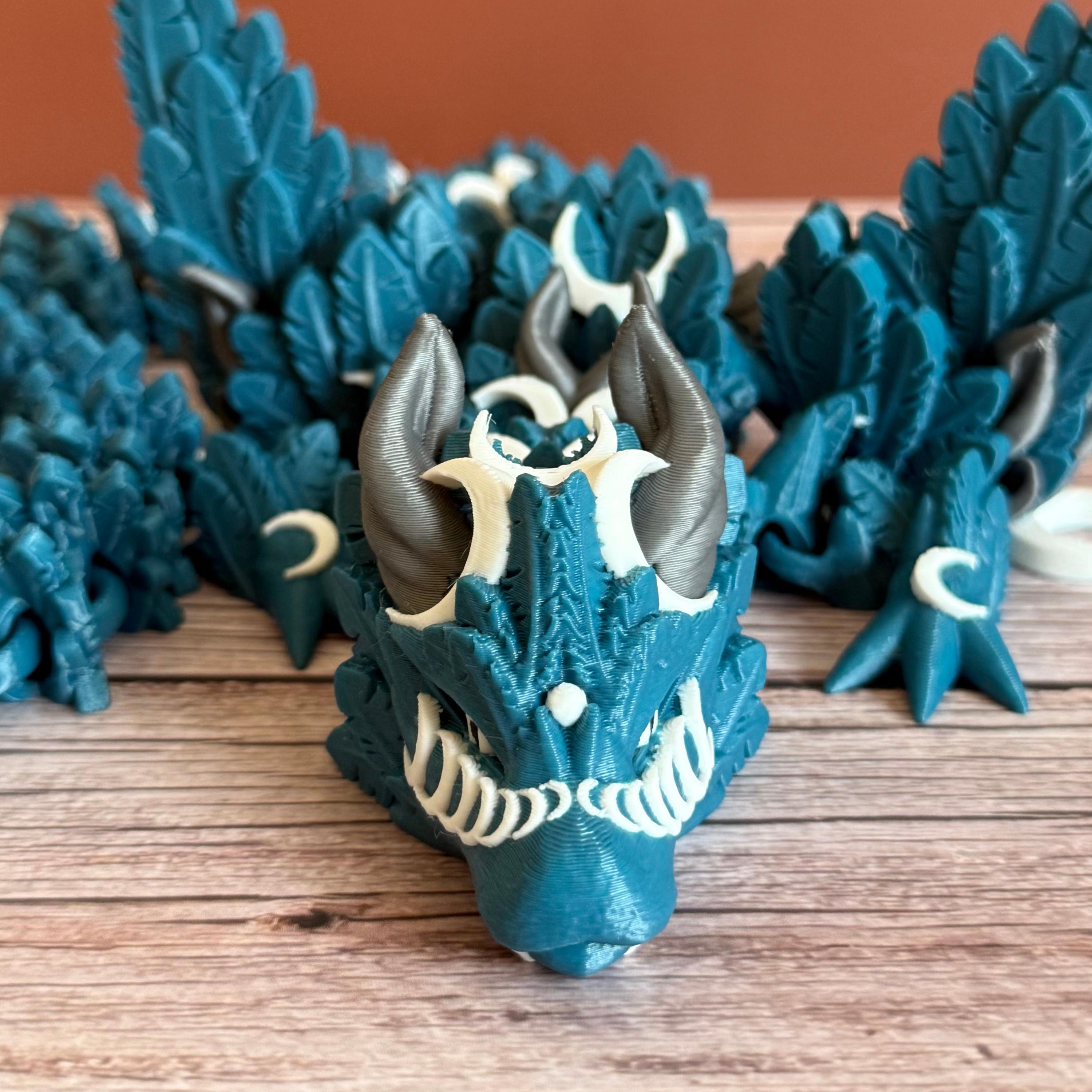 A 3D printed, blue articulated dragon toy with white celestial-inspired patterns, placed on a wooden surface