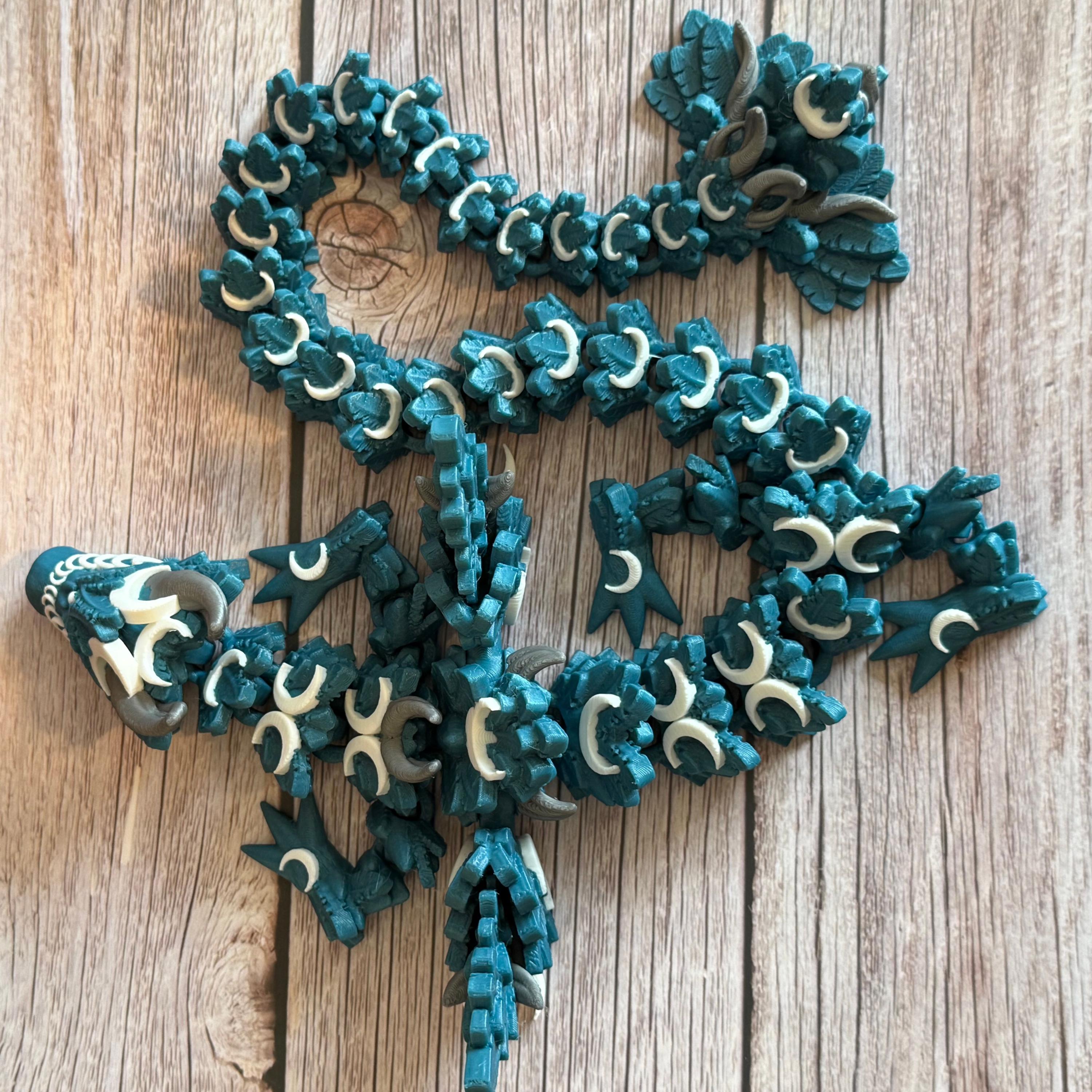 Top of a 3D printed, blue articulated dragon toy with white celestial-inspired patterns, placed on a wooden surface