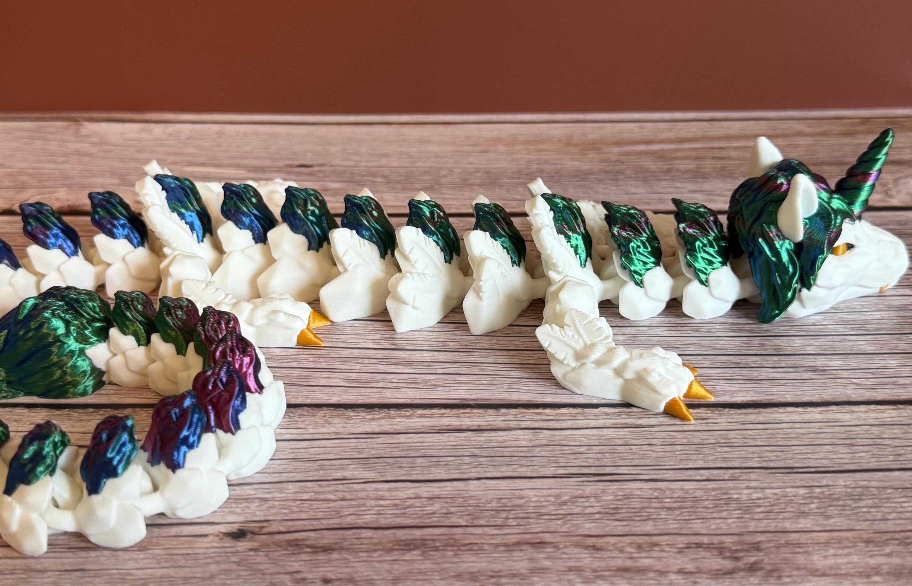Side of a 3D printed white unicorn themed dragon with multicolored mane running the length of the dragon, placed on a wooden surface