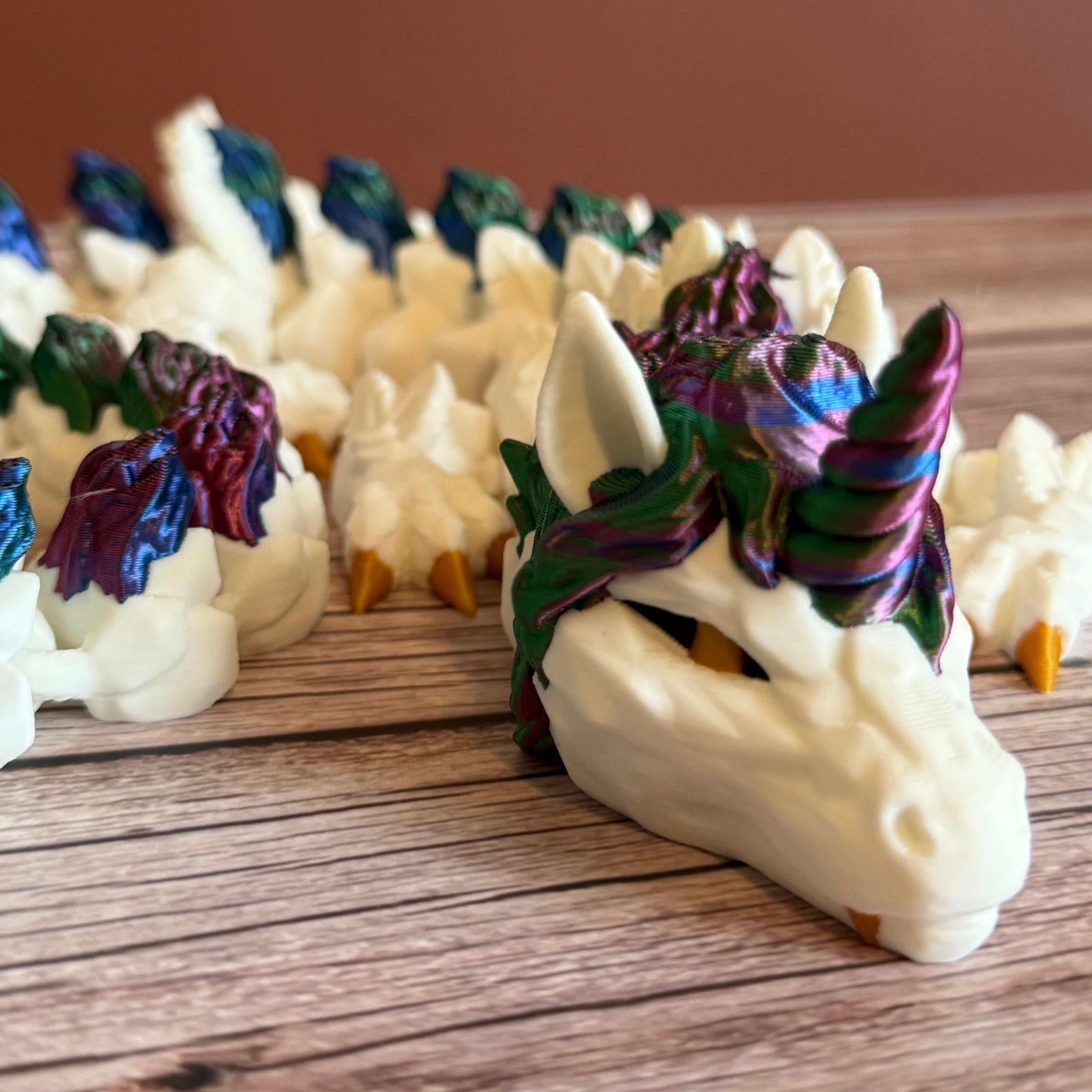 3D printed white unicorn themed dragon with multicolored mane running the length of the dragon, placed on a wooden surface