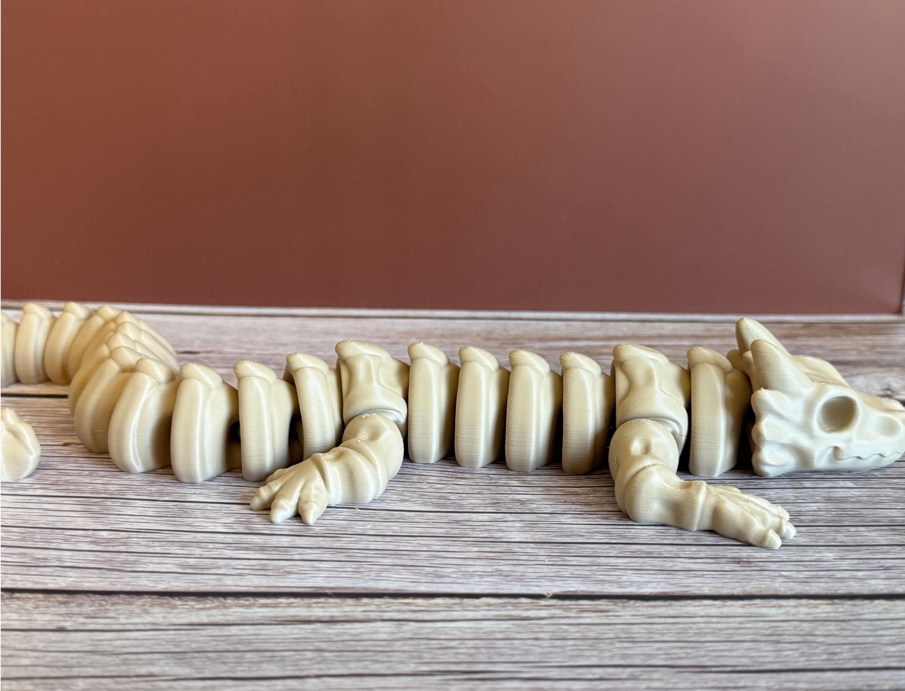 side of a 3D printed beige dragon skeleton toy, placed on a wooden surface