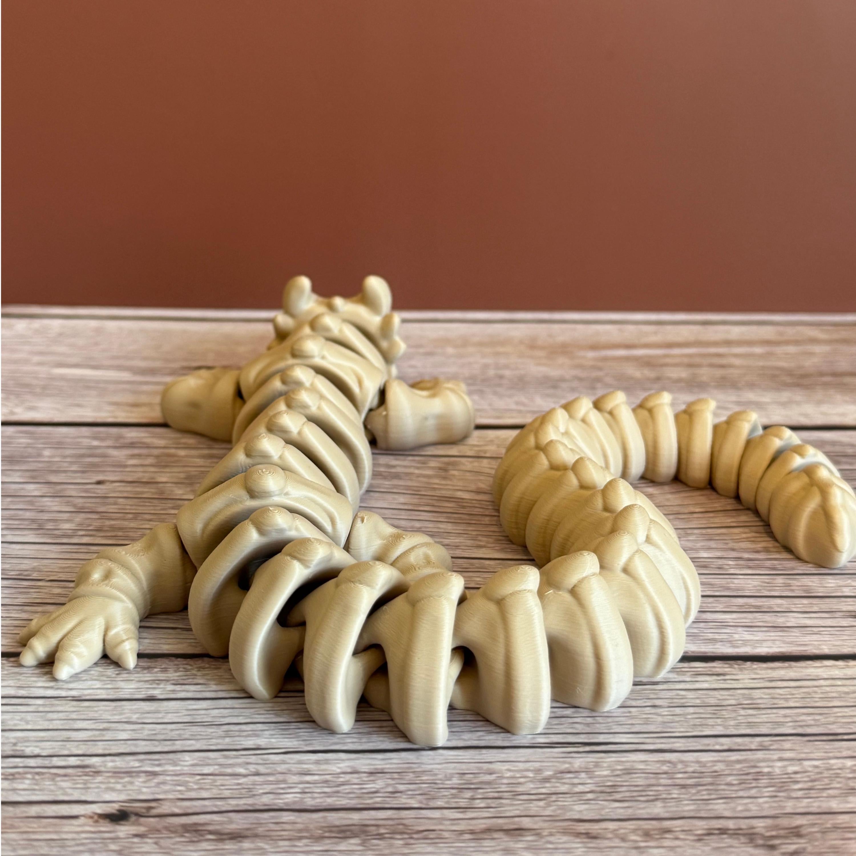 Back of a 3D printed beige dragon skeleton toy, placed on a wooden surface