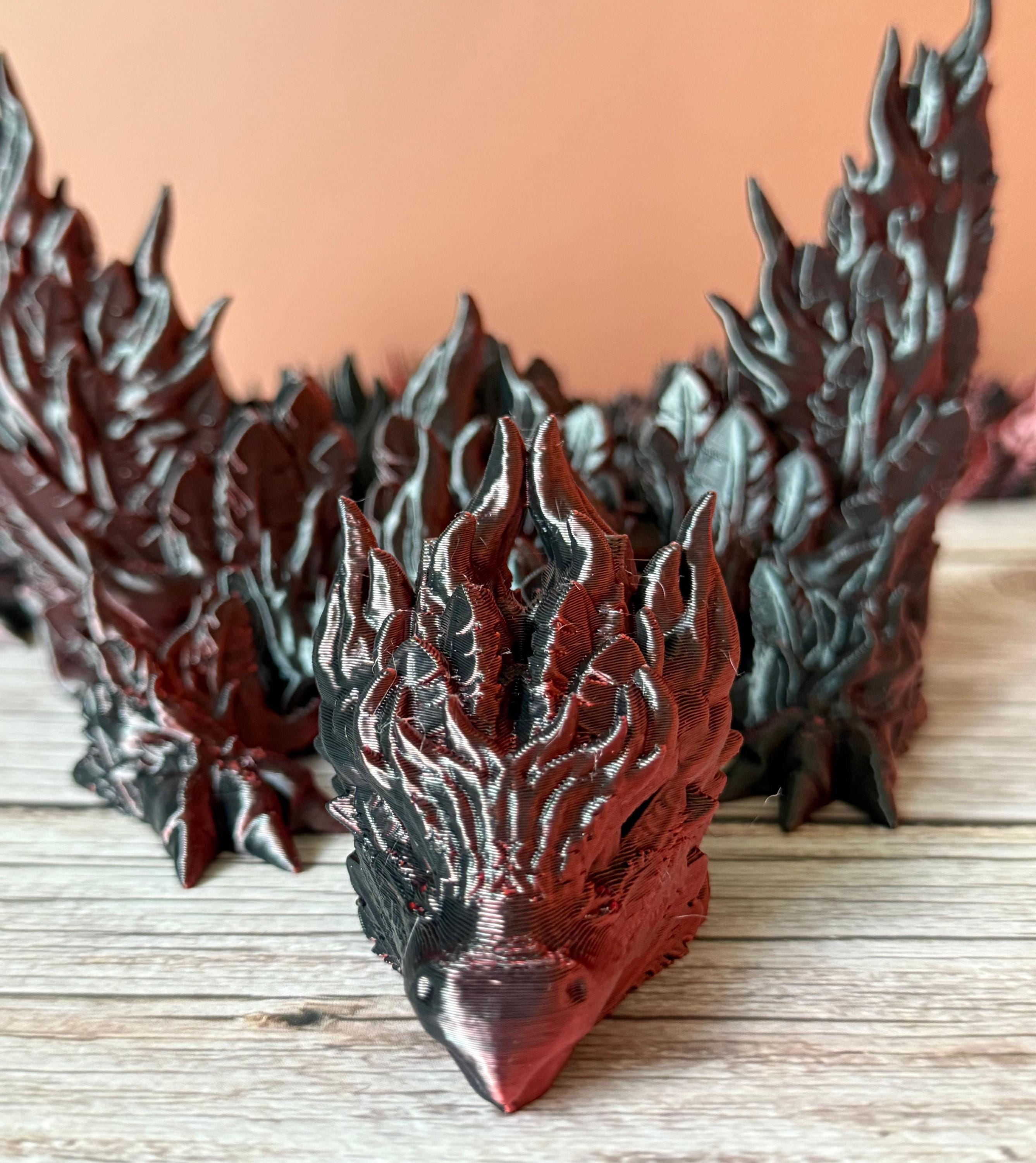 3D printed red and black dragon with flame-like features and wings, placed on a wooden surface
