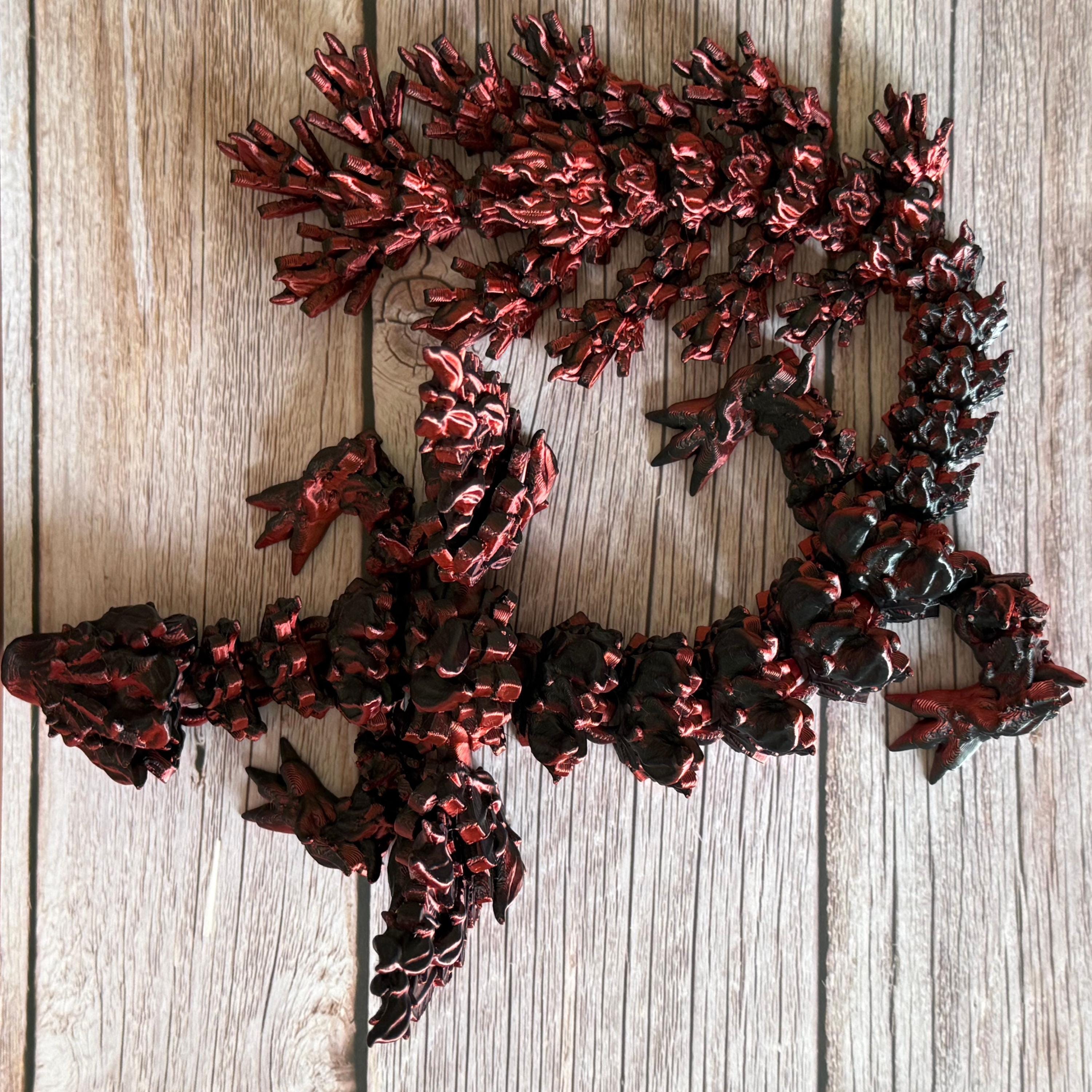 Top of a 3D printed red and black dragon with flame-like features and wings, placed on a wooden surface