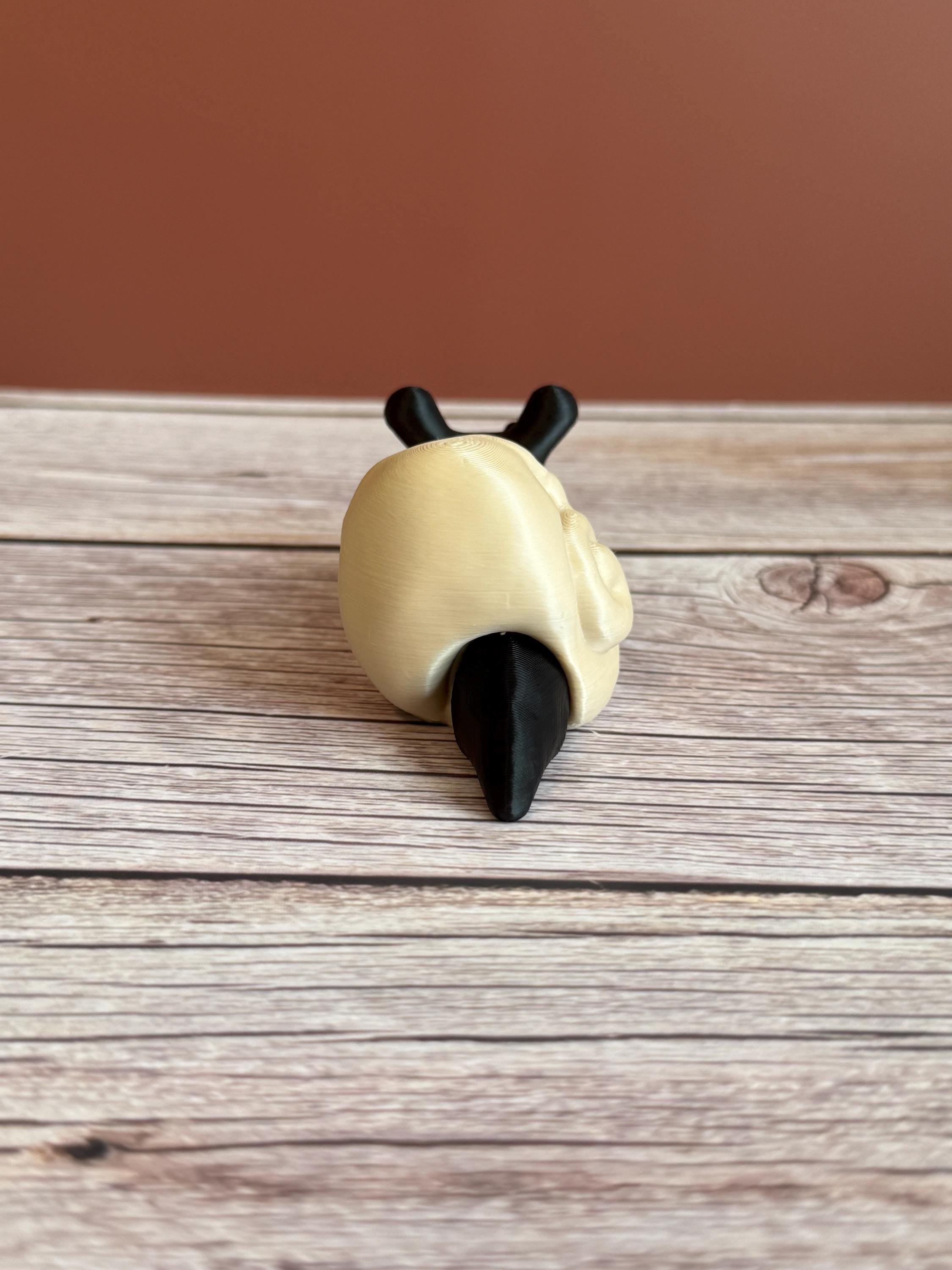 Black 3D printed articulated snail with a beige shell shaped like a human skull, placed on a wooden surface