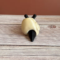 Black 3D printed articulated snail with a beige shell shaped like a human skull, placed on a wooden surface