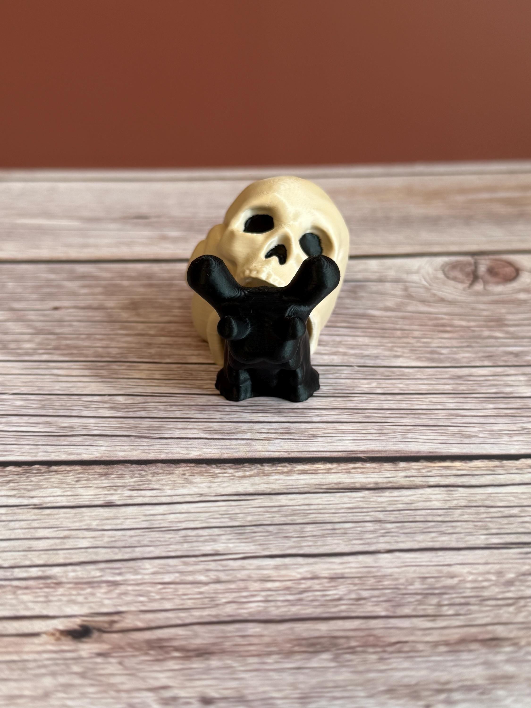 Black 3D printed articulated snail with a beige shell shaped like a human skull, placed on a wooden surface