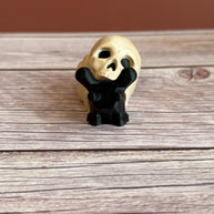 Black 3D printed articulated snail with a beige shell shaped like a human skull, placed on a wooden surface