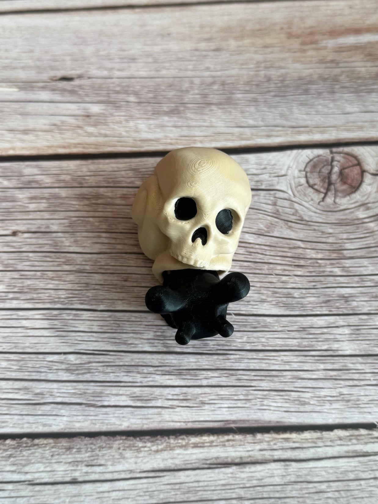 Black 3D printed articulated snail with a beige shell shaped like a human skull, placed on a wooden surface