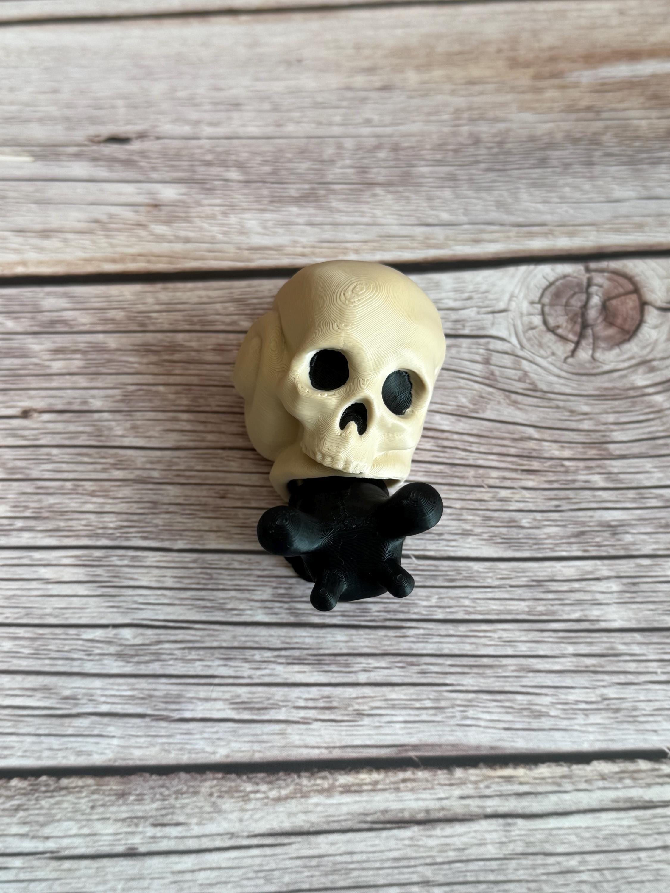 Black 3D printed articulated snail with a beige shell shaped like a human skull, placed on a wooden surface