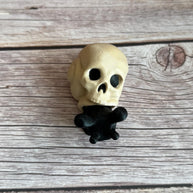 Black 3D printed articulated snail with a beige shell shaped like a human skull, placed on a wooden surface