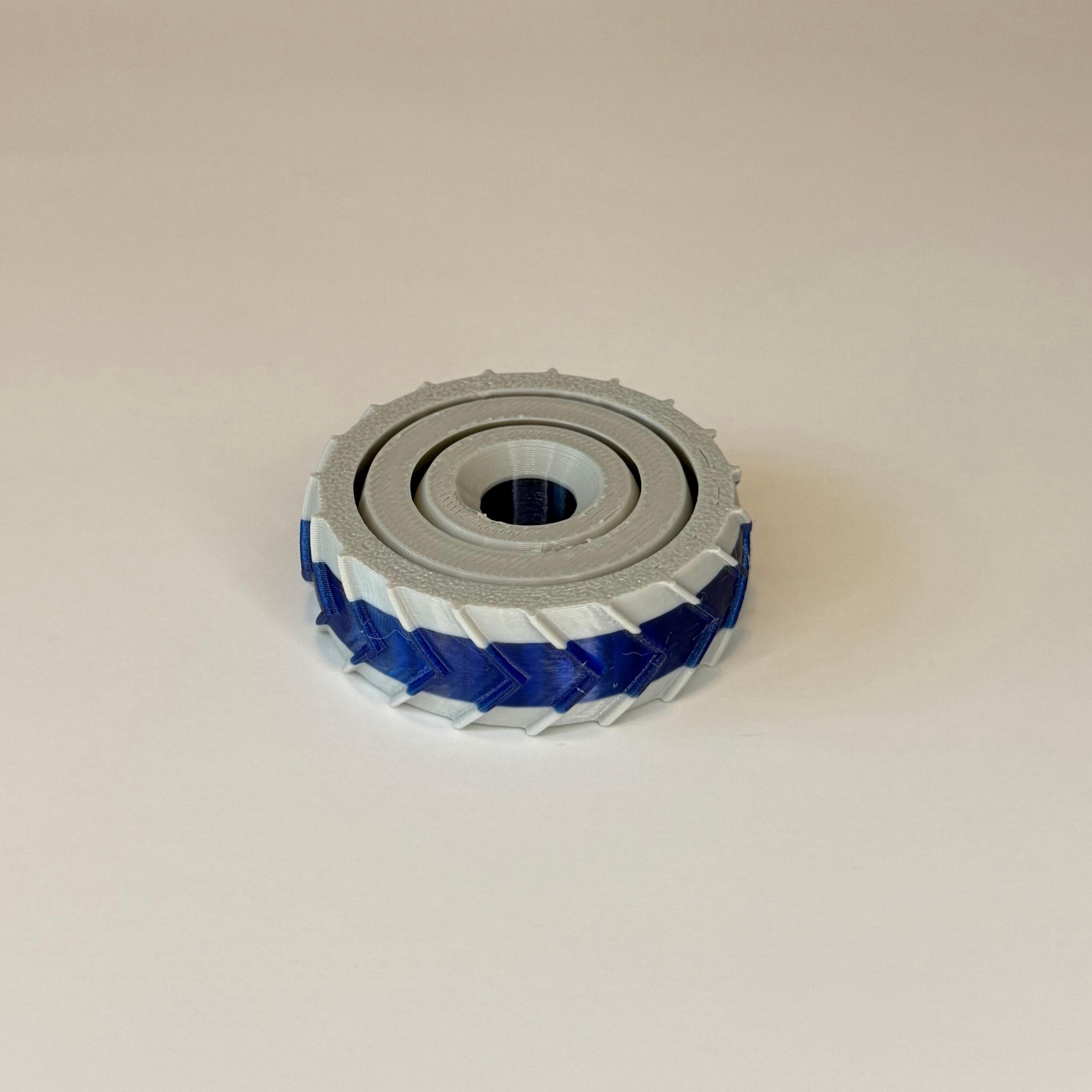 3D printed gray and blue gyro spinner consisting of 3 rings set into each other that spin in different directions on a white background