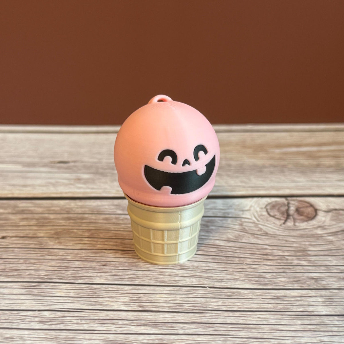 Pink 3D printed ice cream cone keychain with smiling expression on the ice cream scoop.