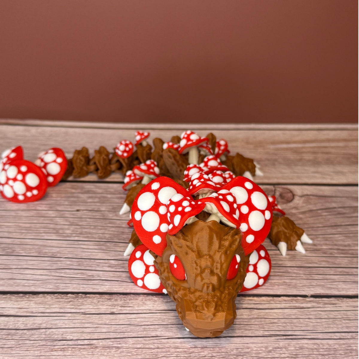 A 12-inch articulated 3D printed dragon with a design resembling a mushroom, with red and white caps on a wooden surface.