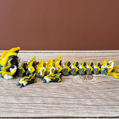 A 3D printed, articulated toy dragon figurine with yellow and black coloring, featuring lightning bolt details and storm cloud patterns, placed on a wooden surface