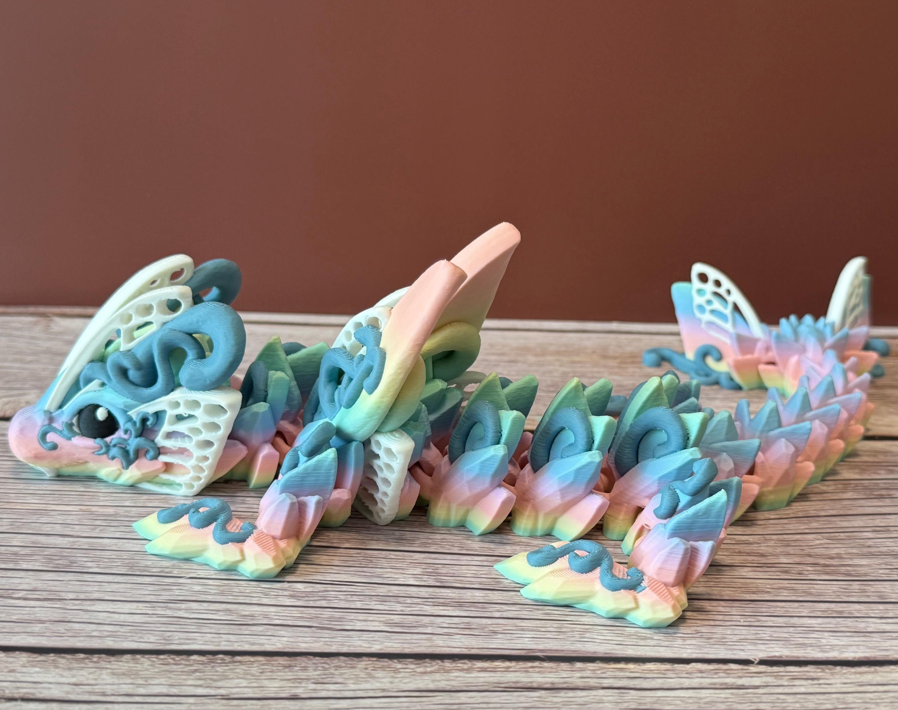 A 3D printed articulated fantasy creature resembling a dragon with butterfly features, in multicolor design, placed on a wooden surface