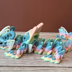 A 3D printed articulated fantasy creature resembling a dragon with butterfly features, in multicolor design, placed on a wooden surface
