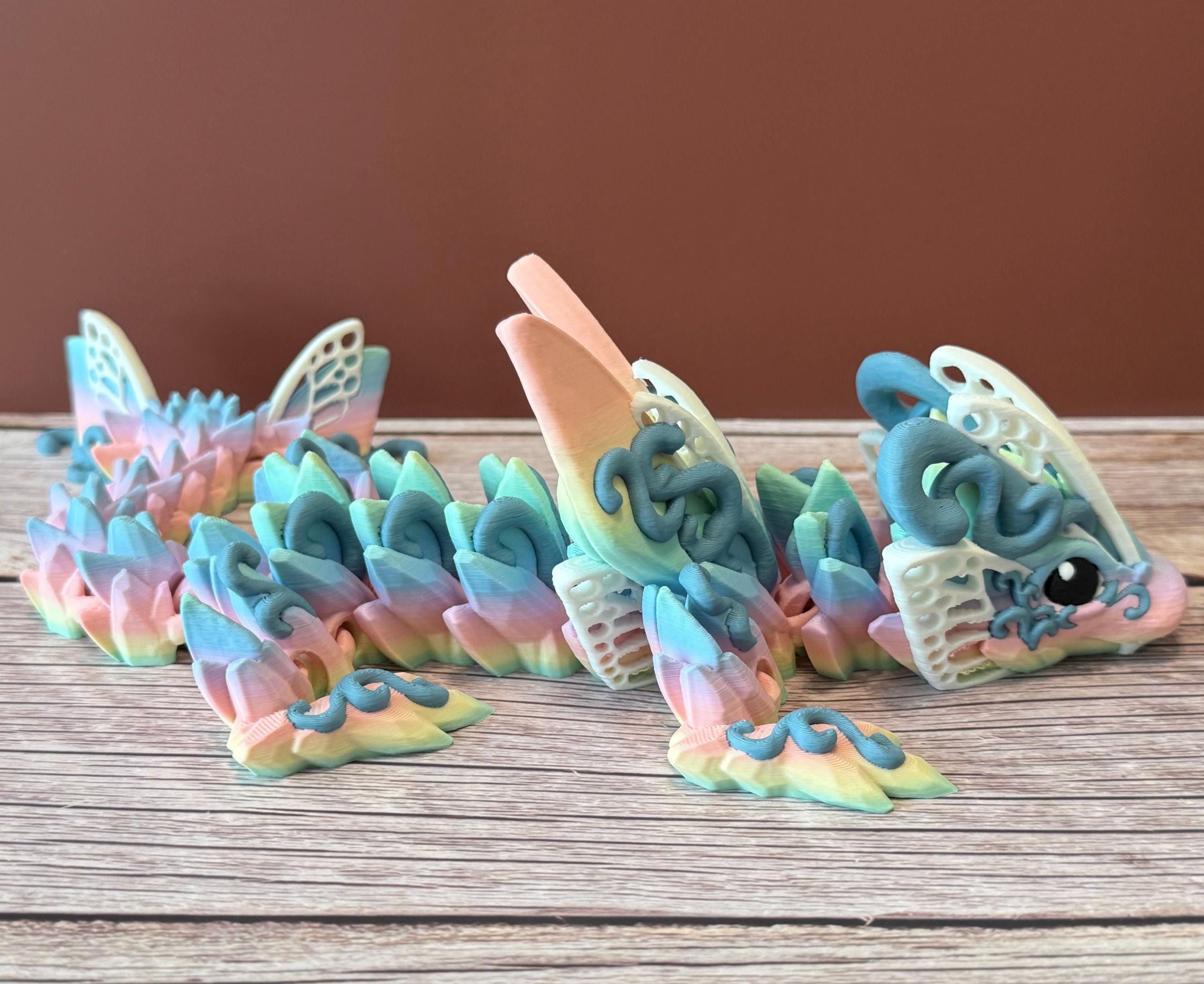 A 3D printed articulated fantasy creature resembling a dragon with butterfly features, in multicolor design, placed on a wooden surface