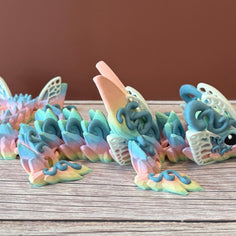 A 3D printed articulated fantasy creature resembling a dragon with butterfly features, in multicolor design, placed on a wooden surface