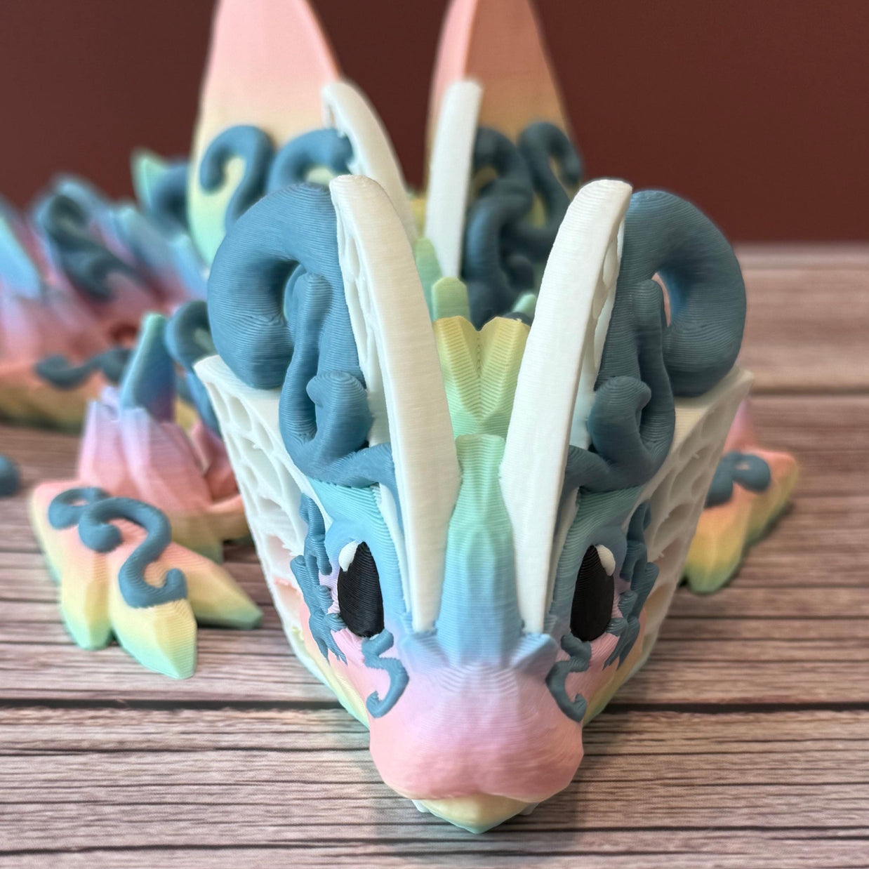 A 3D printed articulated fantasy creature resembling a dragon with butterfly features, in multicolor design, placed on a wooden surface