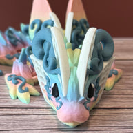 A 3D printed articulated fantasy creature resembling a dragon with butterfly features, in multicolor design, placed on a wooden surface