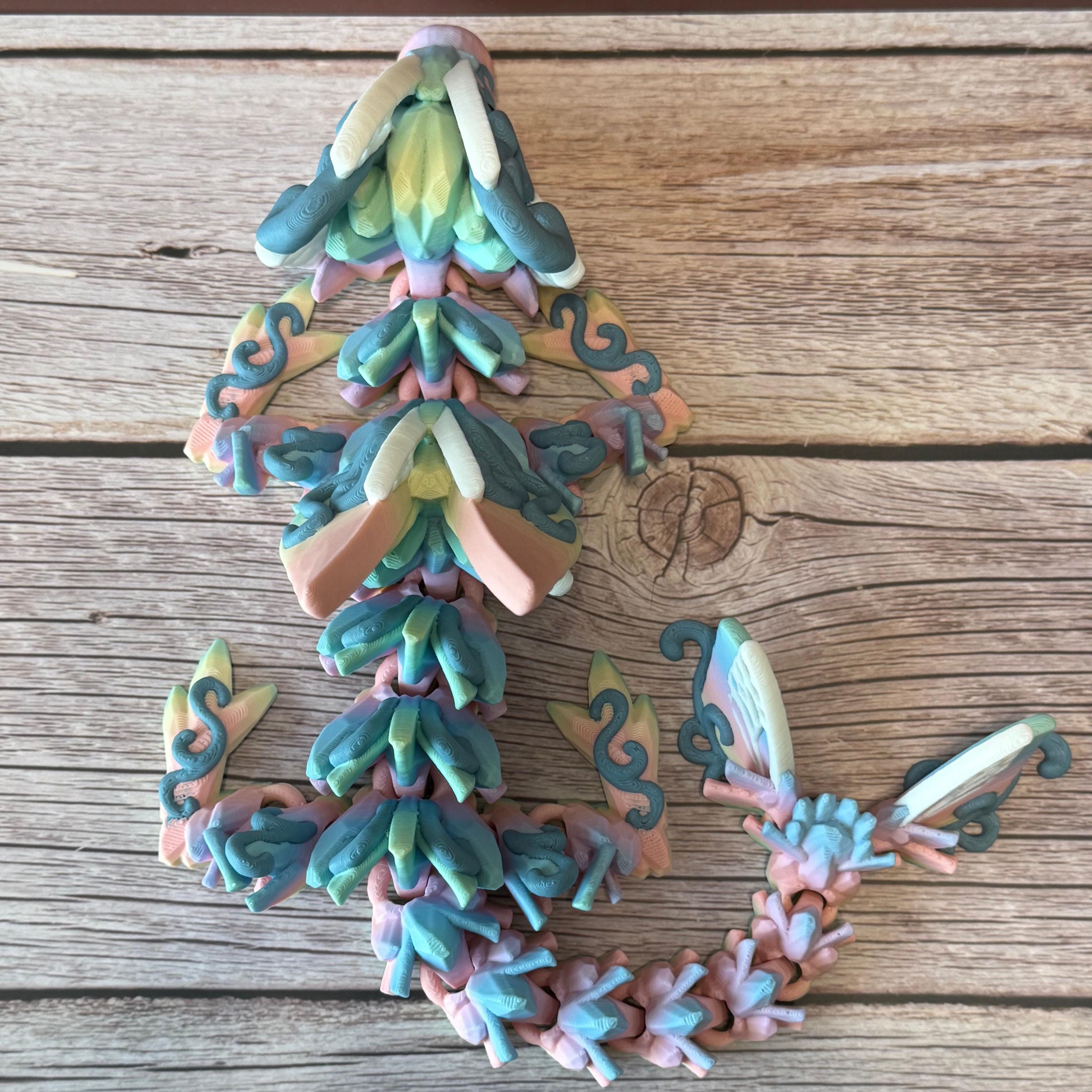 A 3D printed articulated fantasy creature resembling a dragon with butterfly features, in multicolor design, placed on a wooden surface