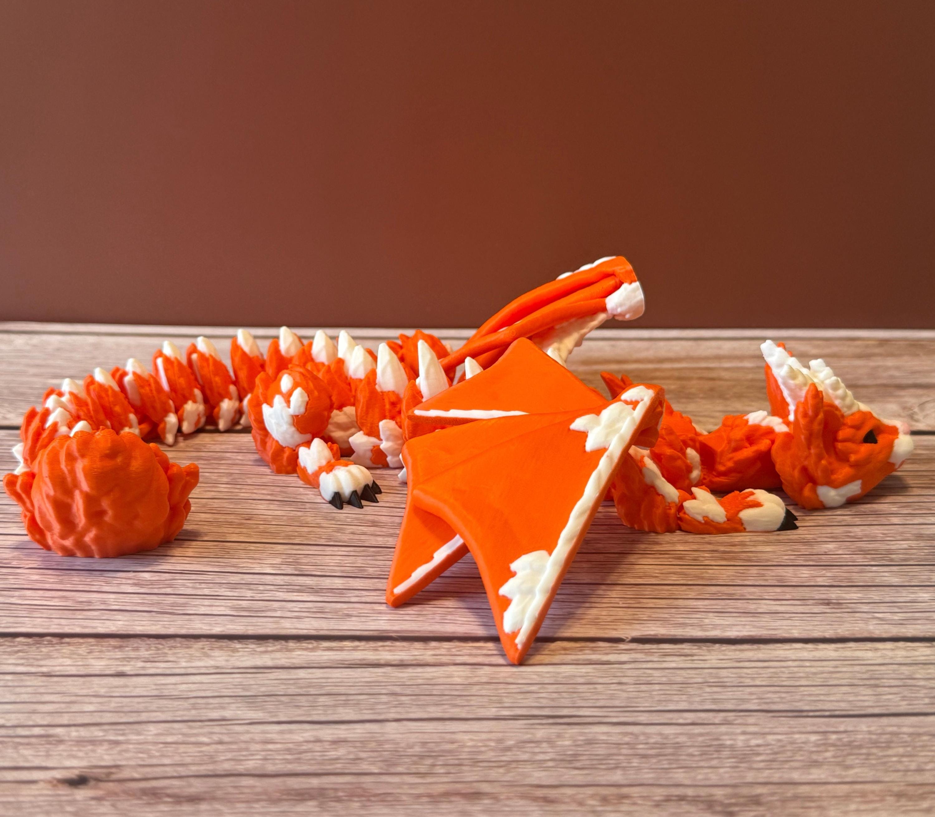 Orange and white 3D printed dragon figurine featuring a hybrid design of a dragon and a cat, placed on a wooden surface