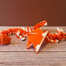 Orange and white 3D printed dragon figurine featuring a hybrid design of a dragon and a cat, placed on a wooden surface