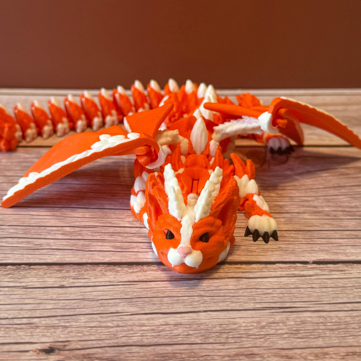 Orange and white 3D printed dragon figurine featuring a hybrid design of a dragon and a cat, placed on a wooden surface