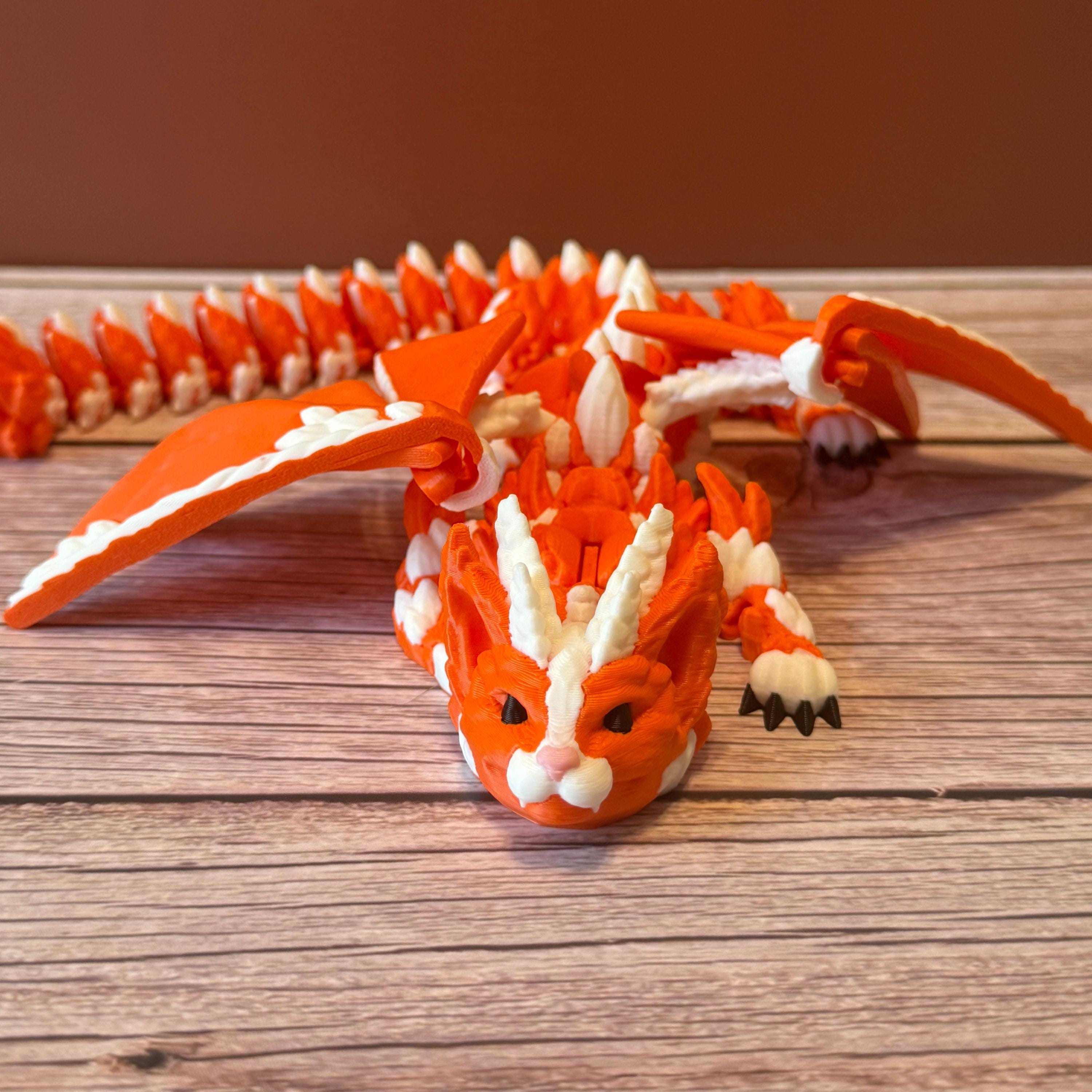 Orange and white 3D printed dragon figurine featuring a hybrid design of a dragon and a cat, placed on a wooden surface