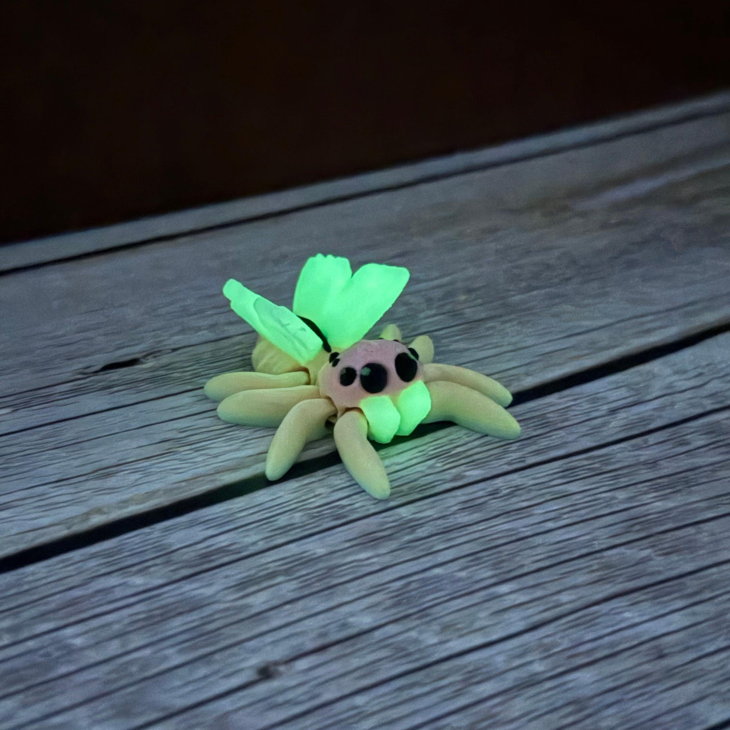 3D printed small spider with fairy design featuring rainbow coloring and glowing wings, placed on a wooden surface