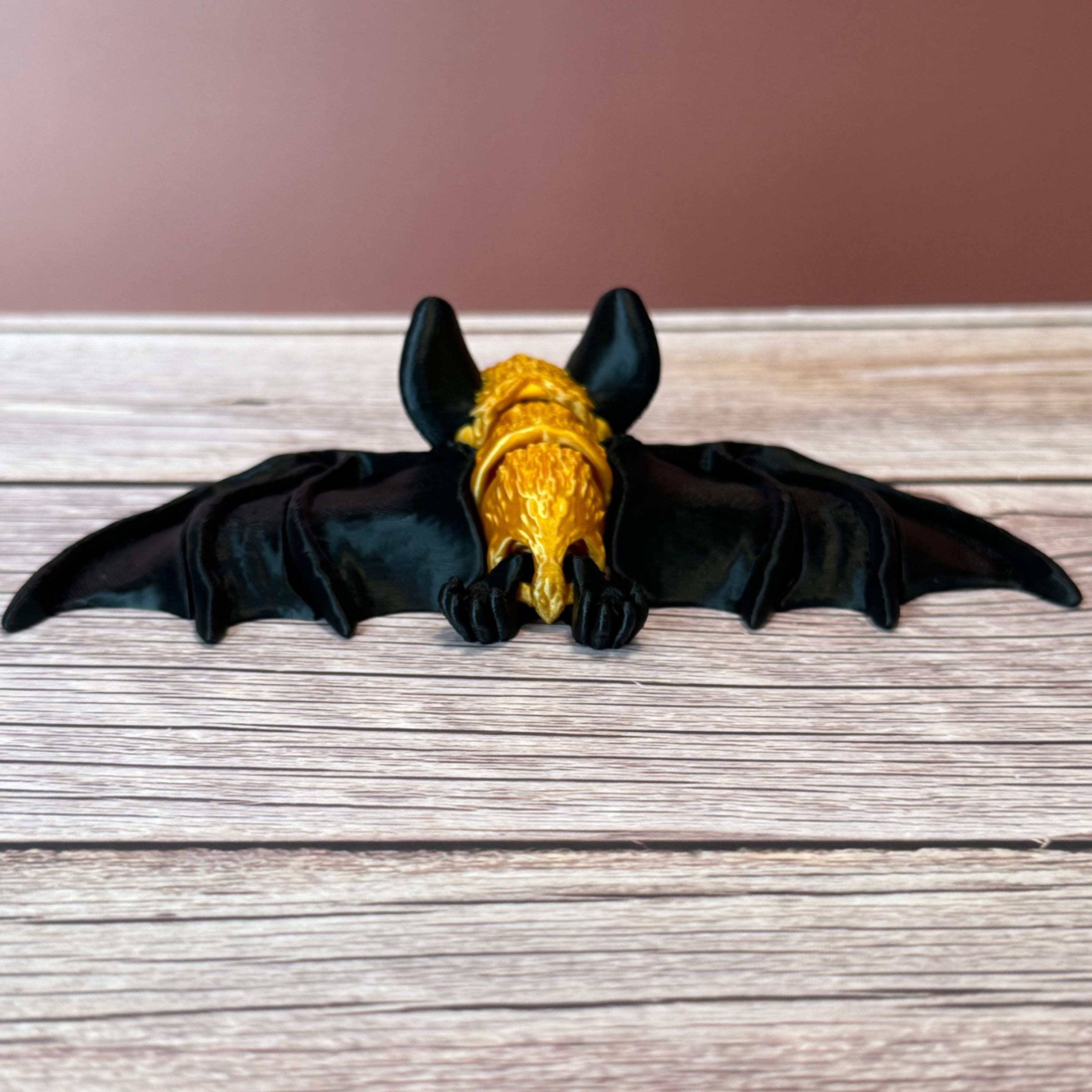 3D printed gold and black articulated bat, placed on a wooden surface
