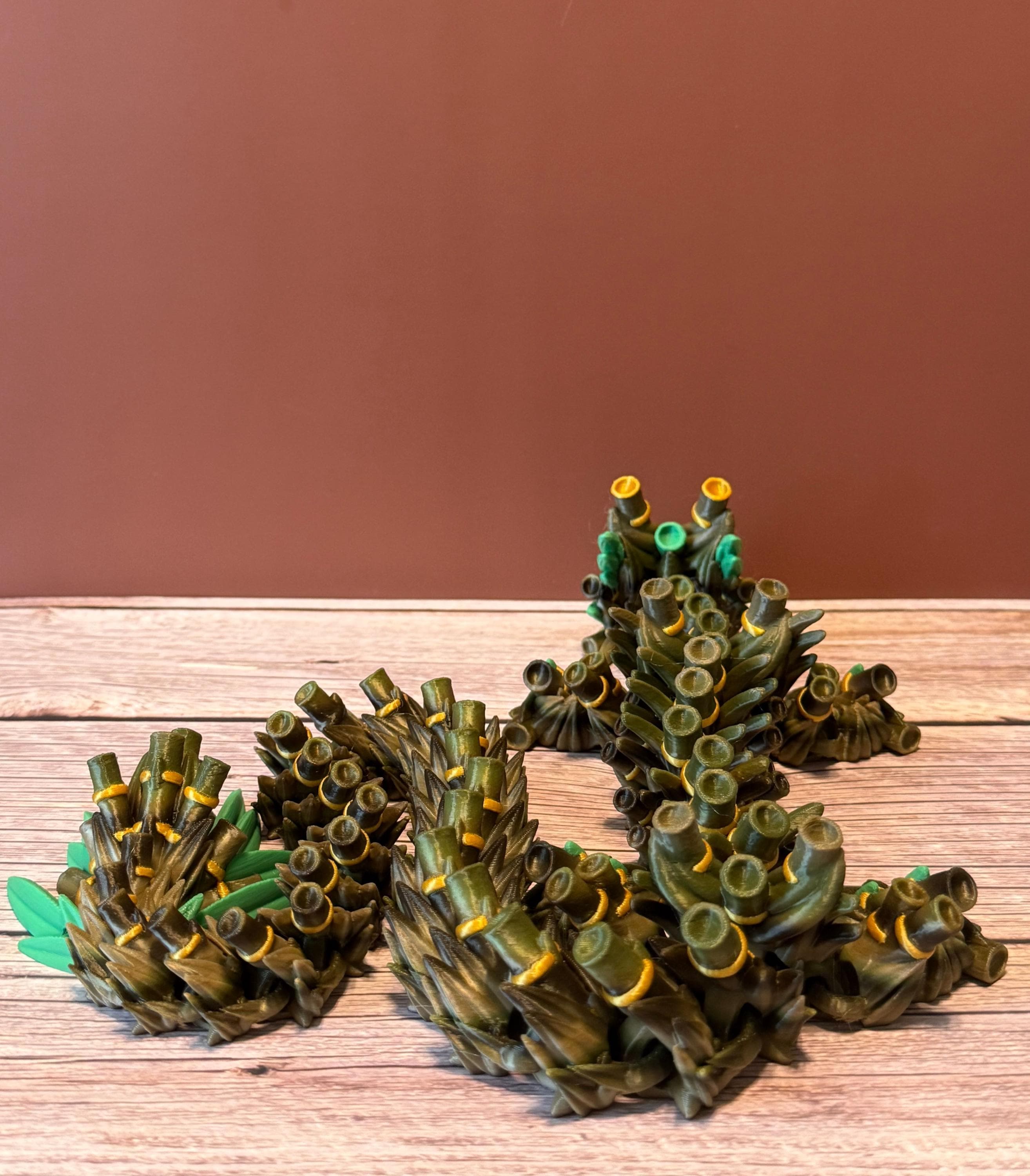 A green, brown, and gold colored 3D printed dragon figure with bamboo-like features, placed on a wooden surface