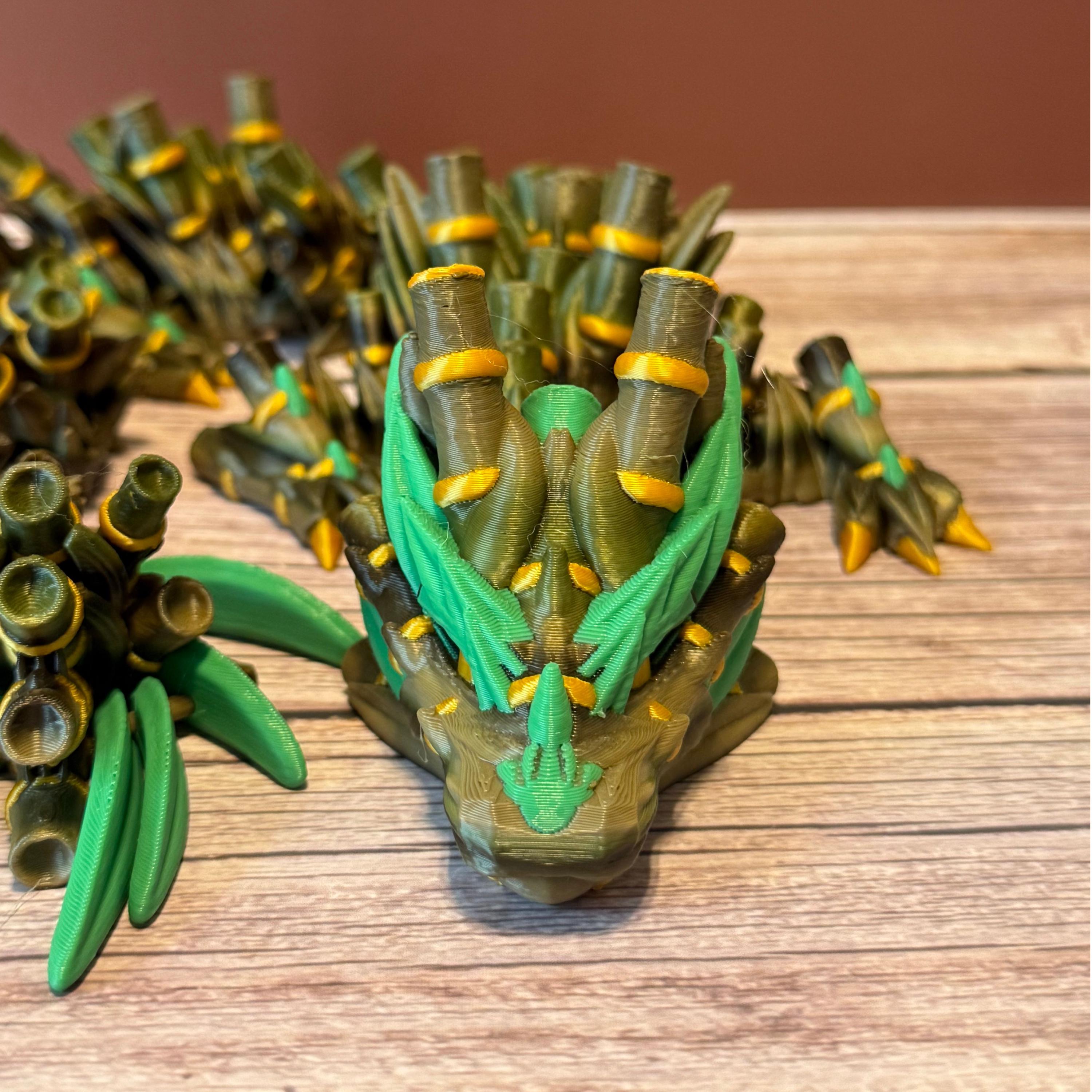 A green, brown, and gold colored 3D printed dragon figure with bamboo-like features, placed on a wooden surface