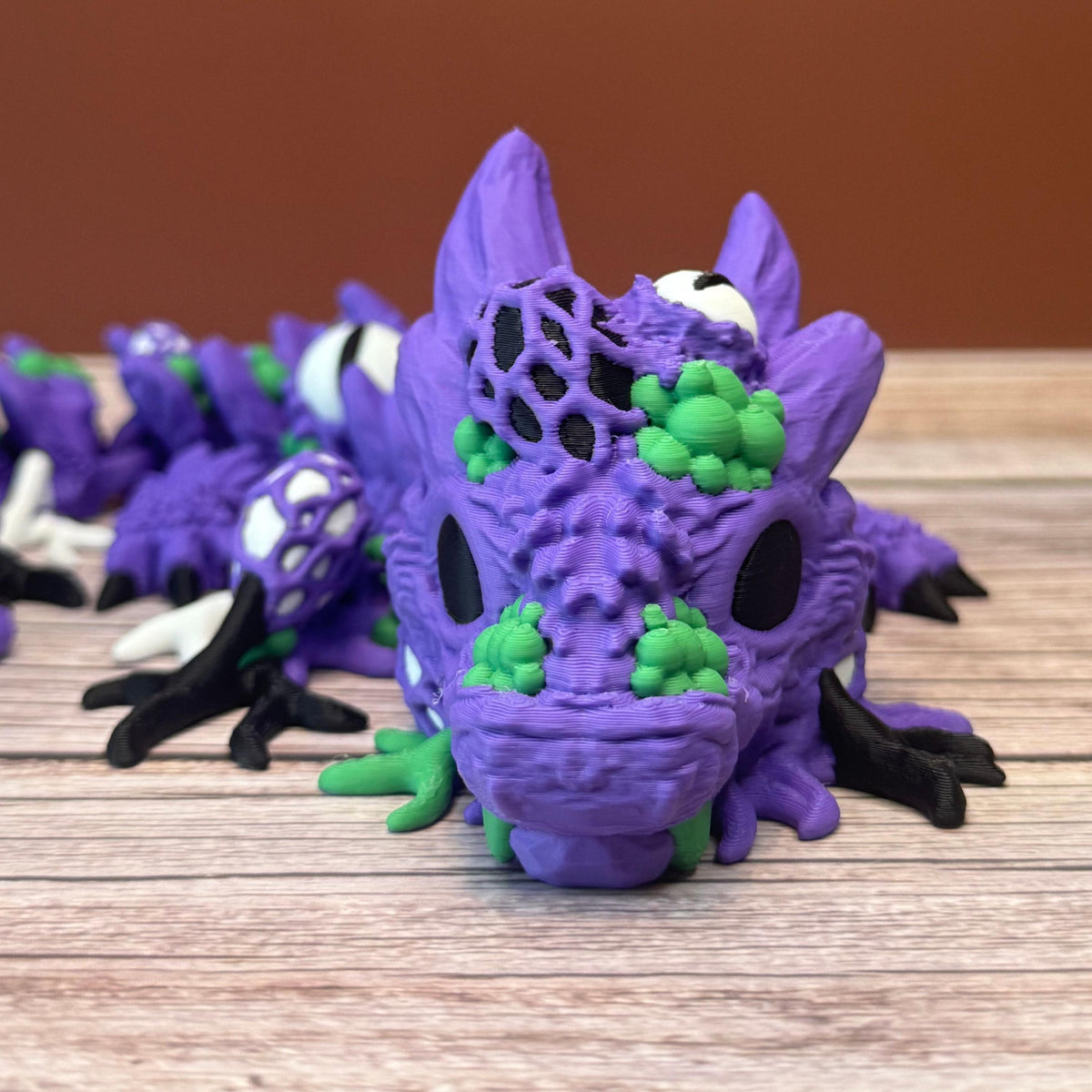 Purple and green 3D printed dragon with multiple eyes and growth-like features all over its body, placed on a wooden surface