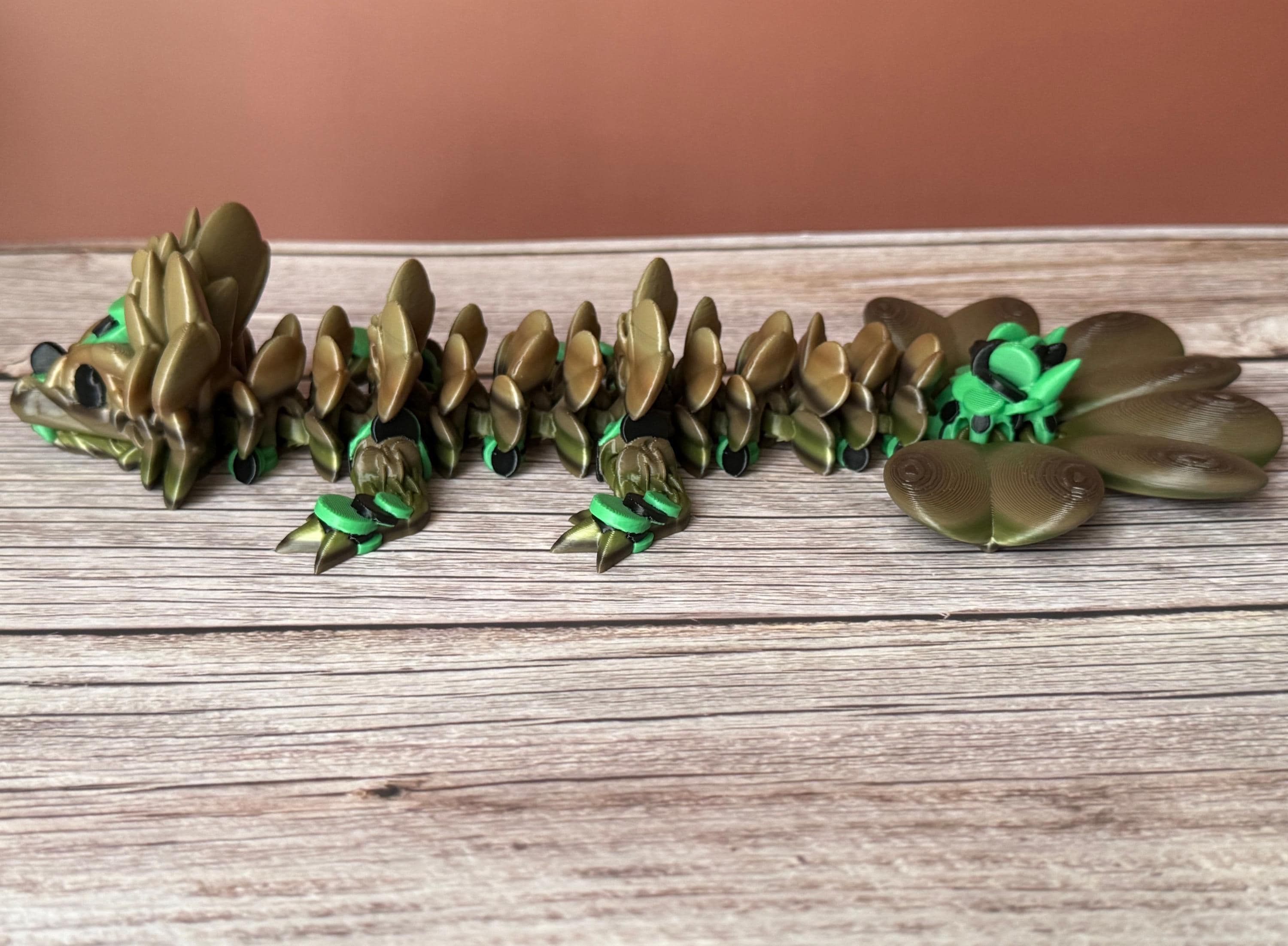 Brown and green 3D printed dragon figure with a clover shaped tail, placed on a wooden surface